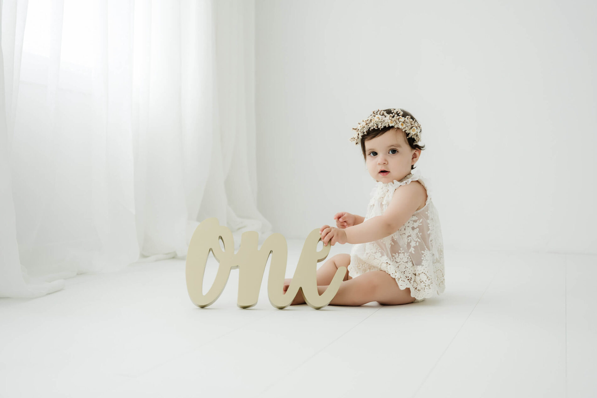 One-year-old girl sitting beside a wooden “one” sign during a Seattle first birthday milestone photo session.