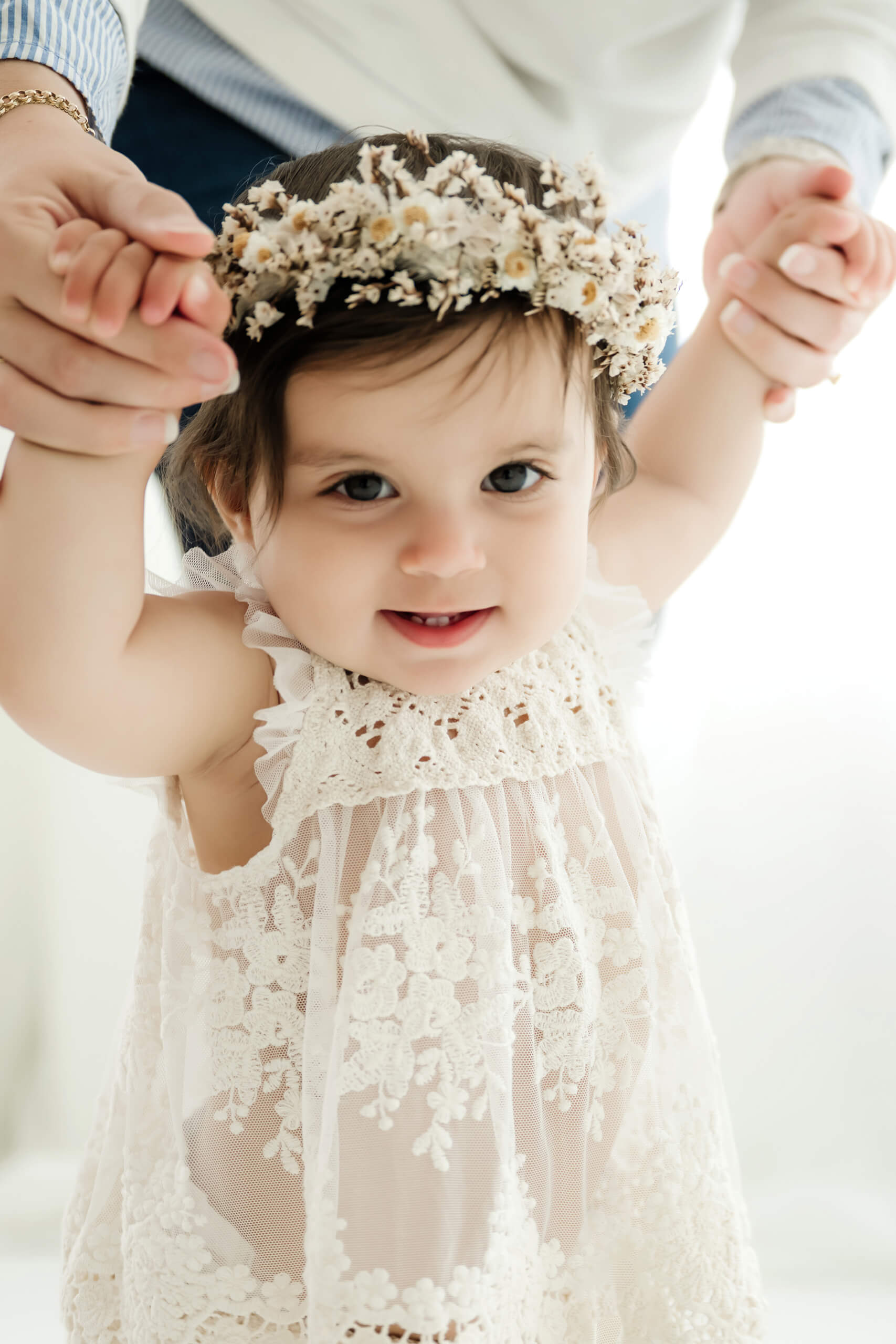 Baby girl smiling while holding her parents’ hands during a first birthday milestone photo session near Seattle.