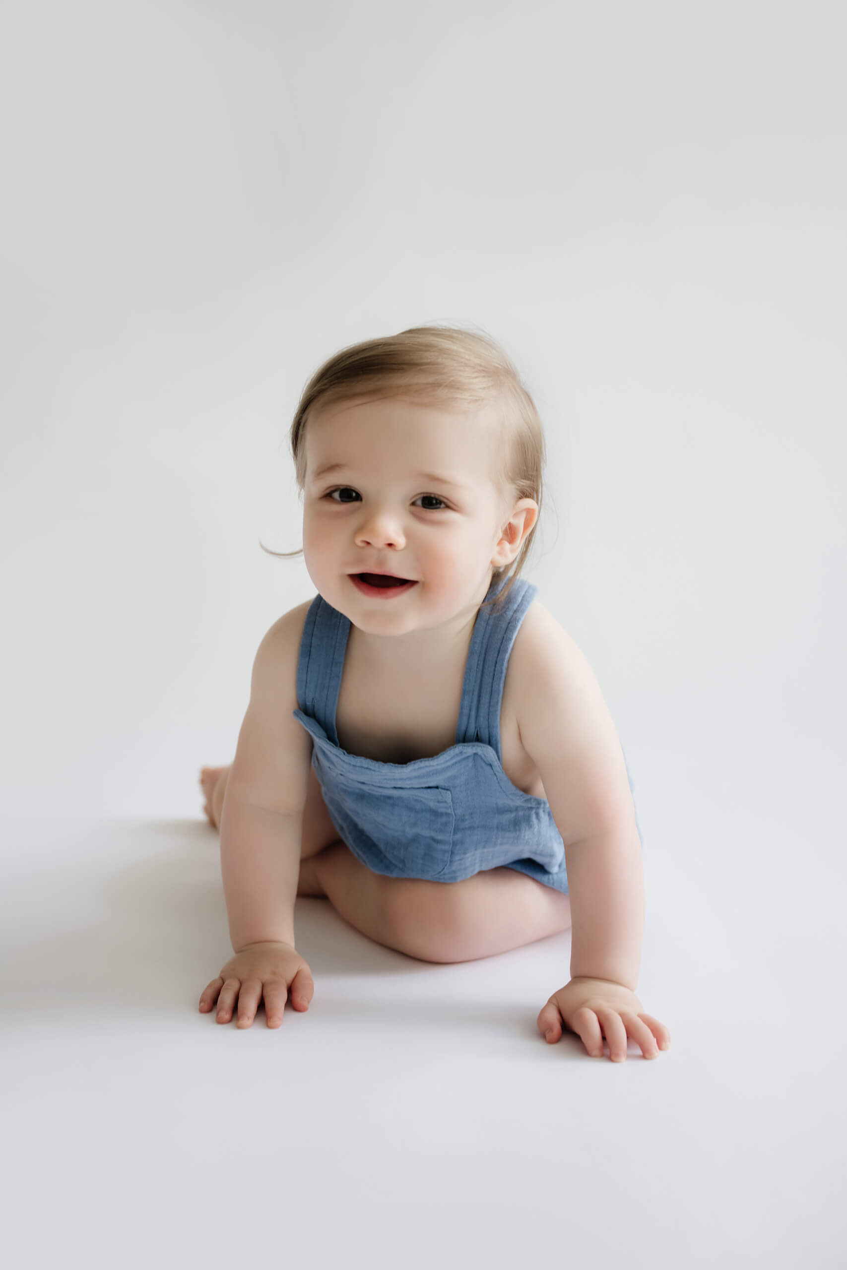 One-year-old crawling in a blue romper during a first birthday milestone photo session at a bright Kirkland studio near Seattle.