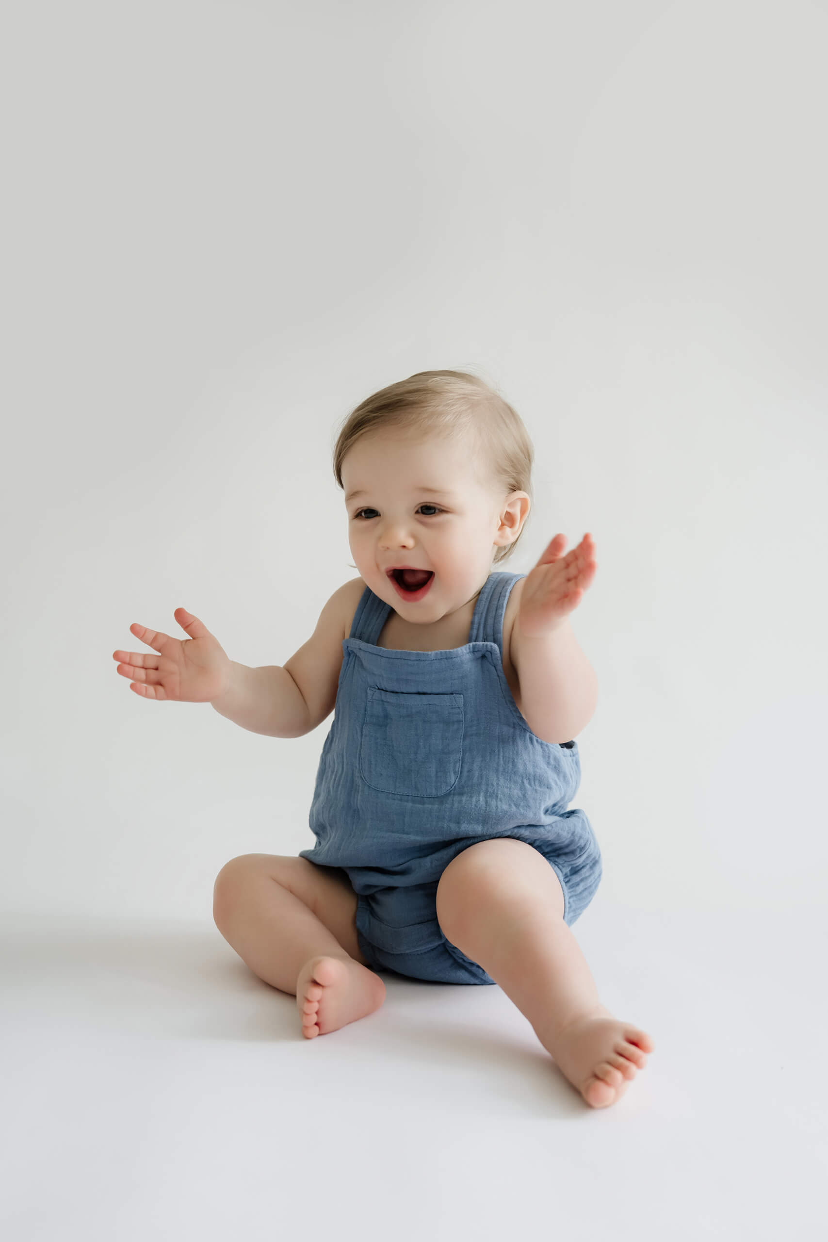 Smiling one-year-old clapping during a first birthday milestone photography session in a bright white studio.