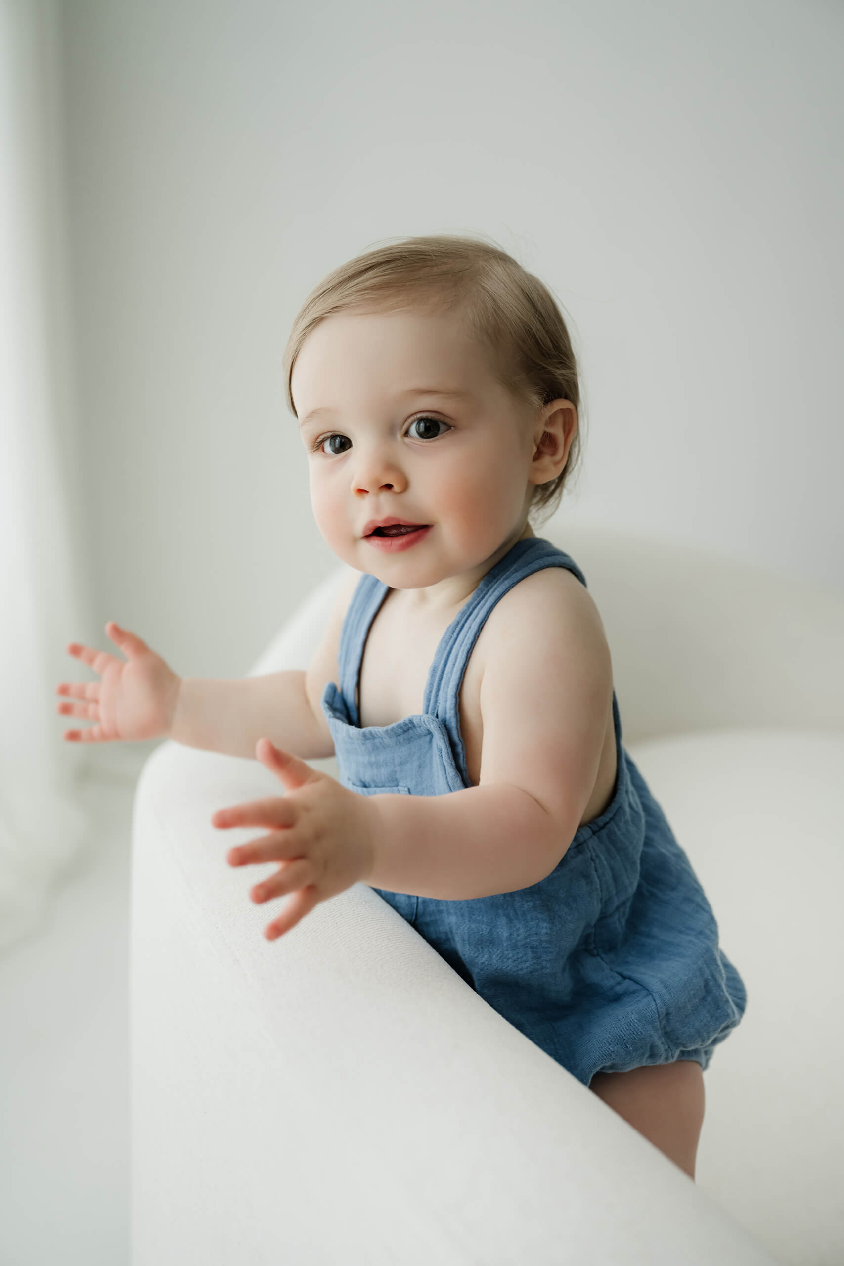 One-year-old standing beside a white studio chair during a Seattle first birthday milestone session.