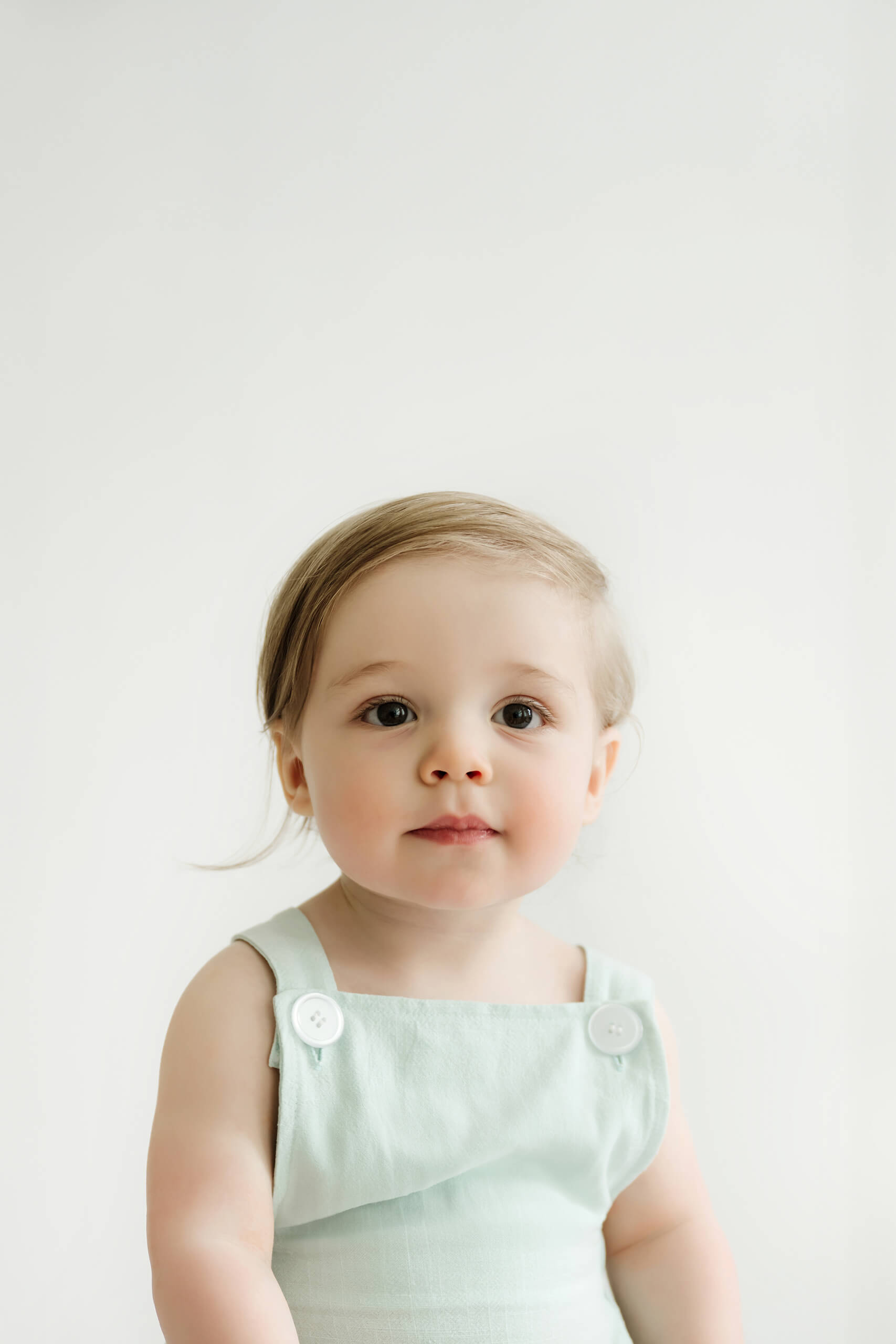 Close-up first birthday portrait of a one-year-old in a light green outfit at a Kirkland photography studio.
