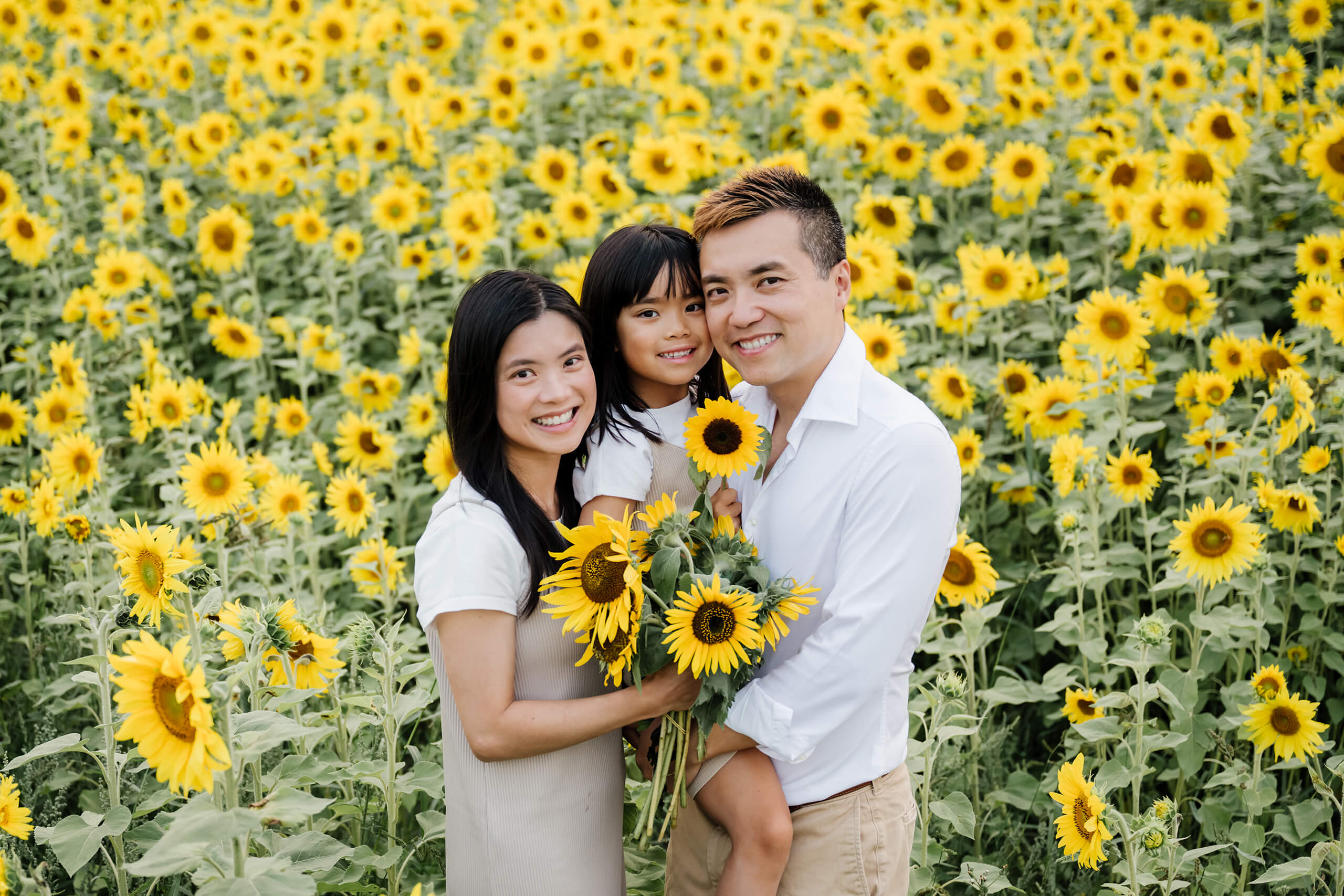 Family of three smiling together in a sunflower field during a Seattle-area summer photo session.