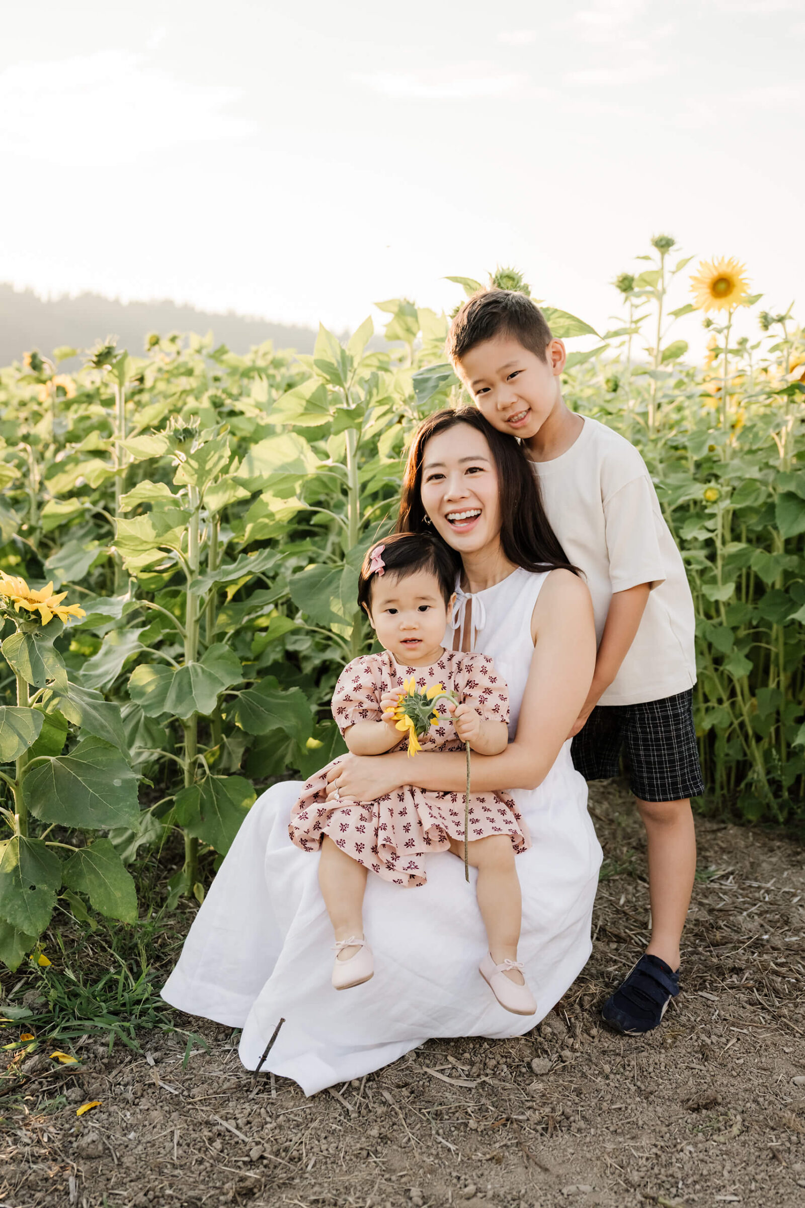 Mother seated with her baby daughter and young son during a family sunflower field session near Seattle.