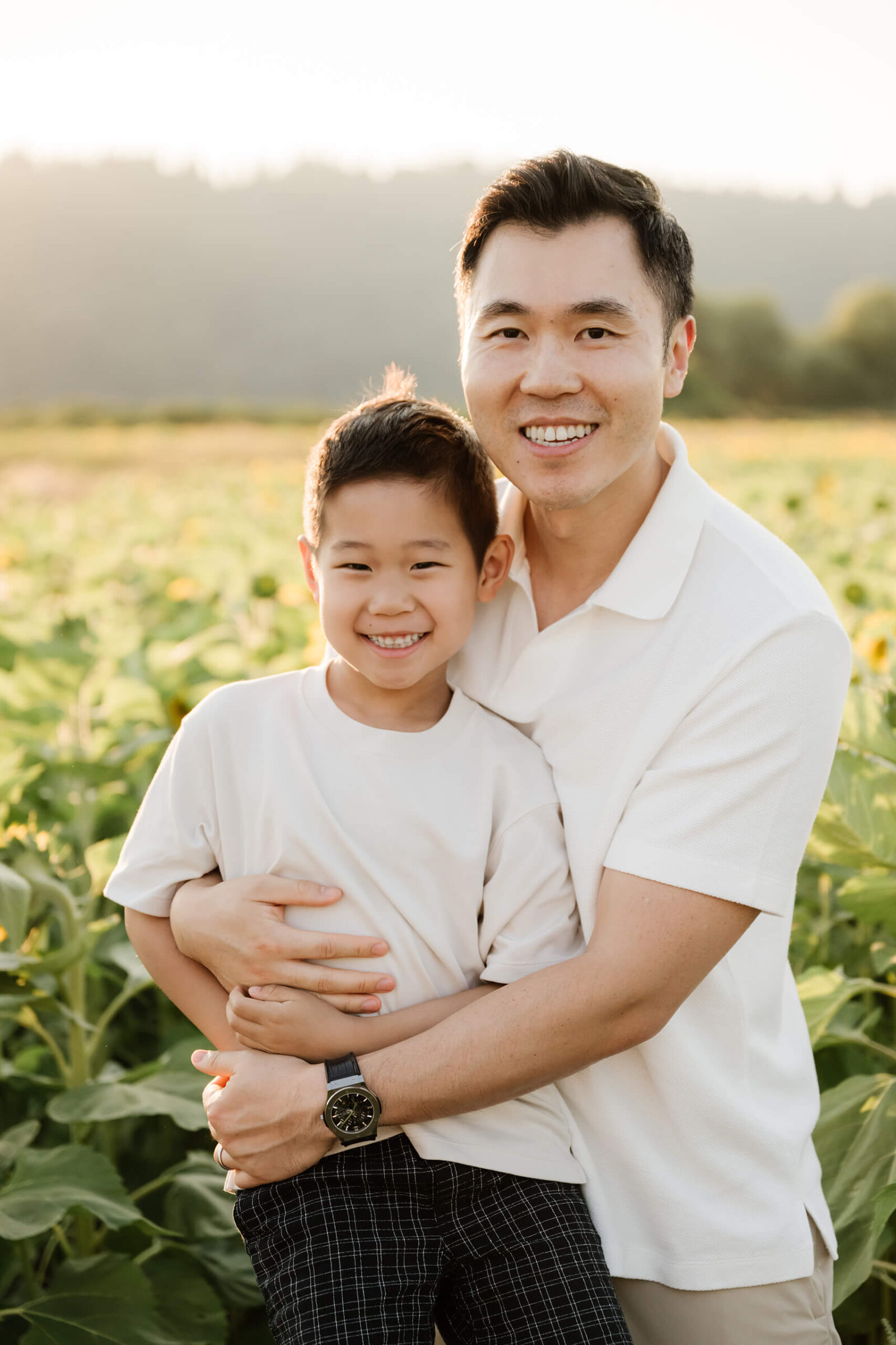 Father hugging his young son during a sunset family photo session in a sunflower field near Seattle.