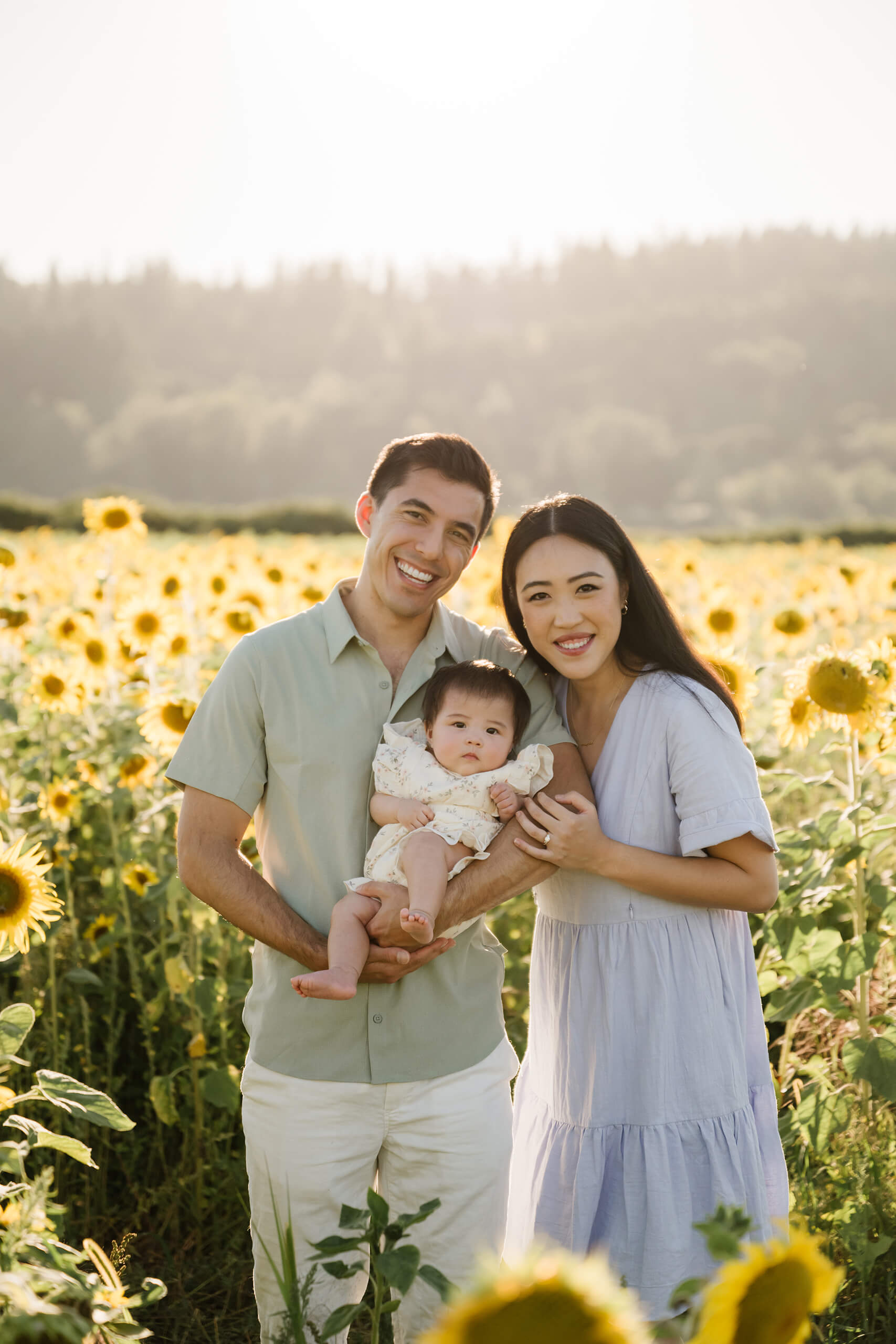 Mother and father holding their baby for a family portrait among glowing sunflowers near Seattle.