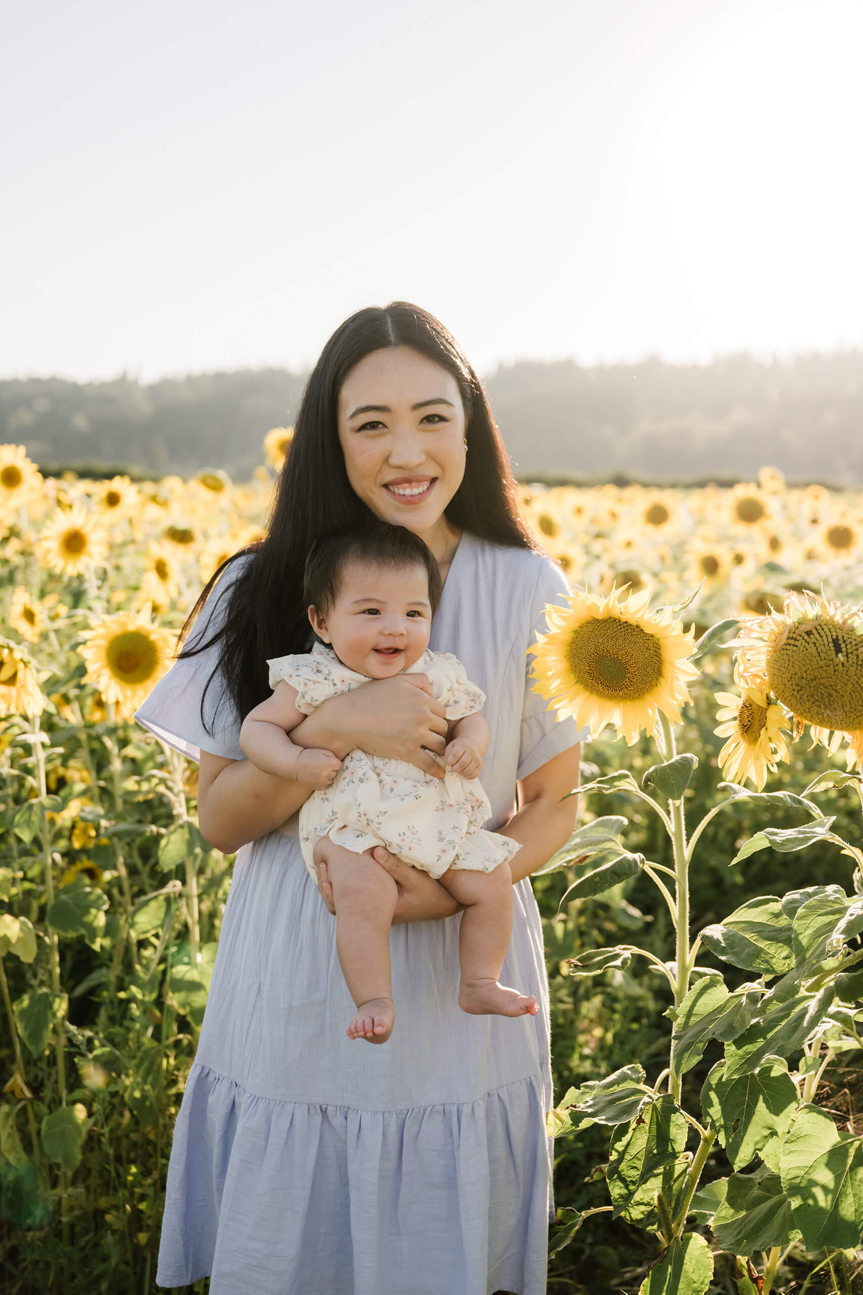 Mother holding her smiling baby among sunflowers during a summer family session near Seattle.