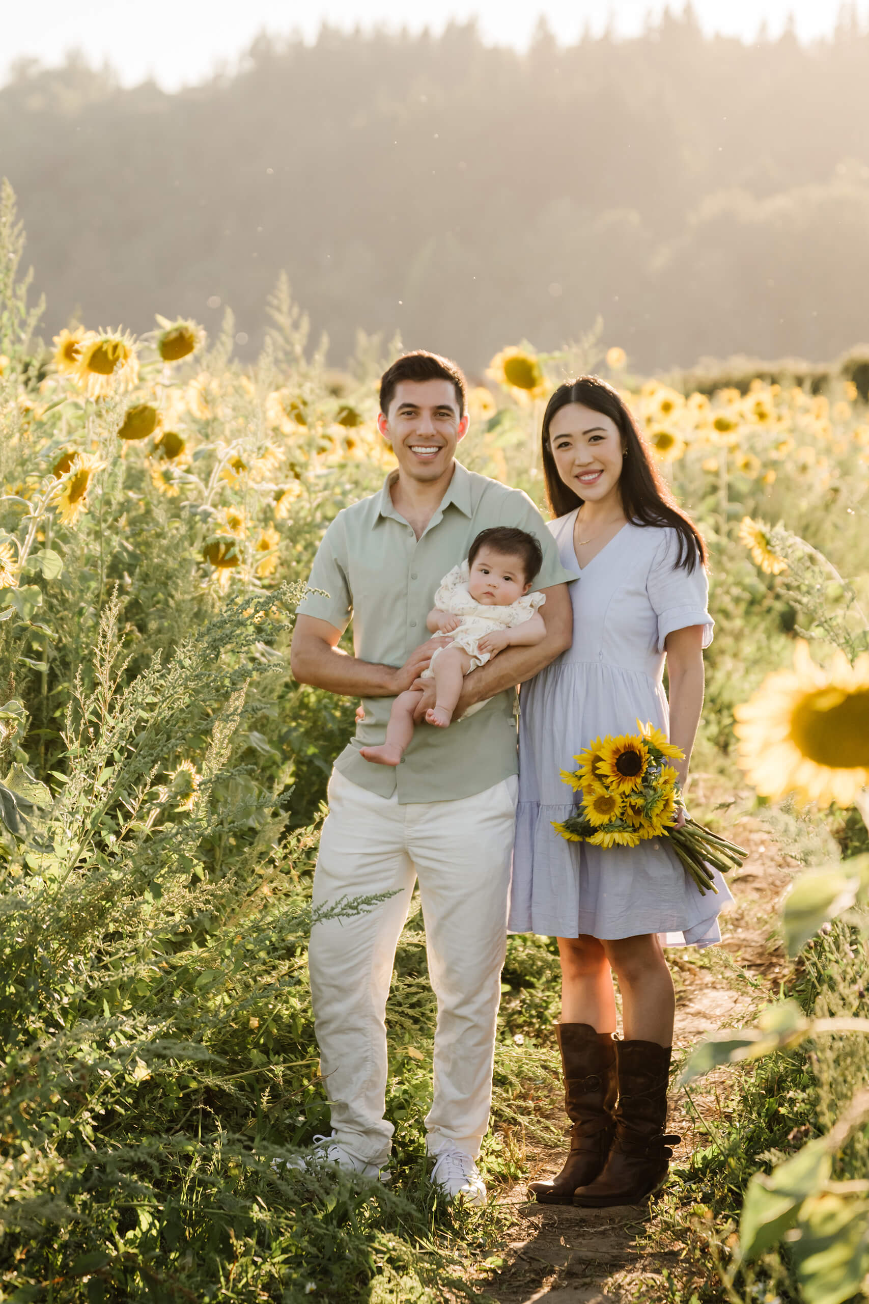 Family of three posing with their baby and a sunflower bouquet during a golden-hour session in Duvall.