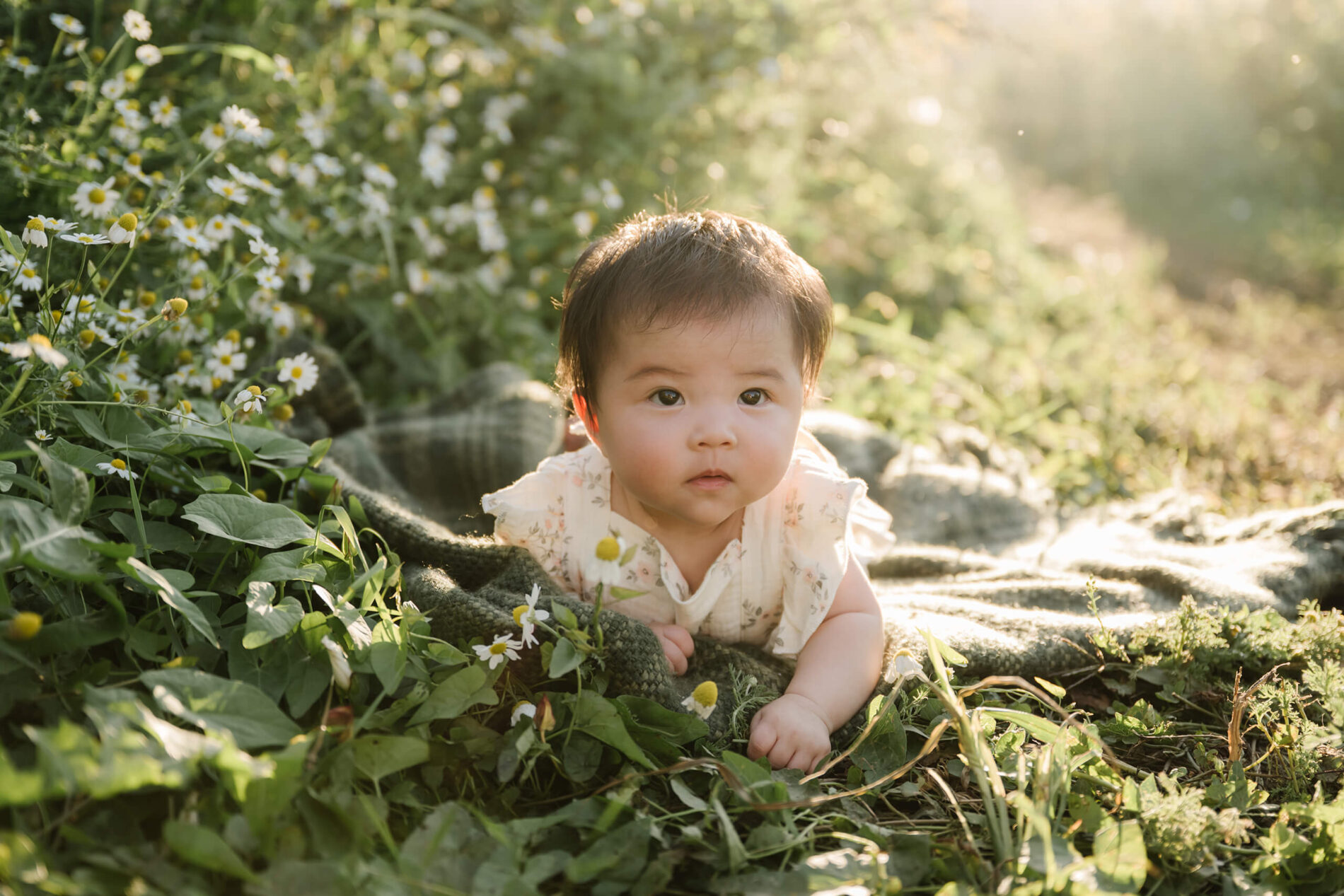 Baby lying on a blanket beside small white flowers during a summer family photo session in Duvall.