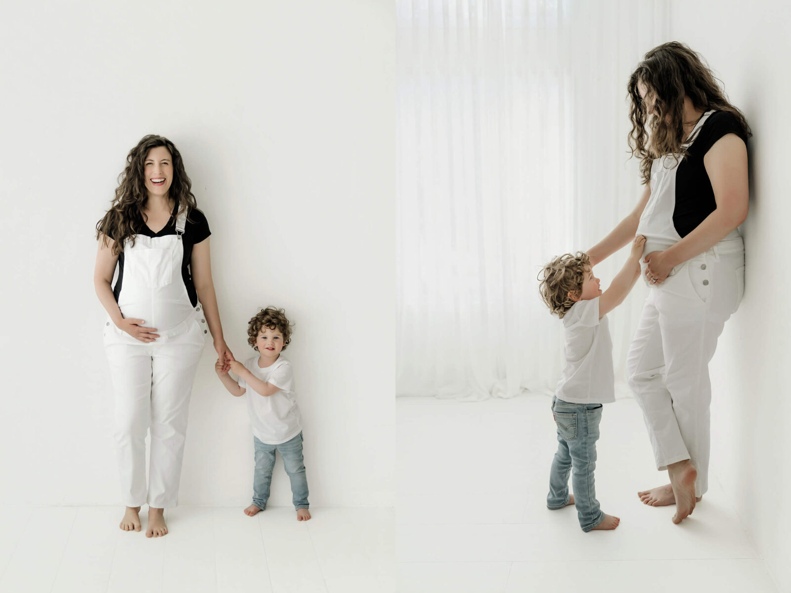 Pregnant woman holding hands and playing with her young child in a bright white maternity studio.