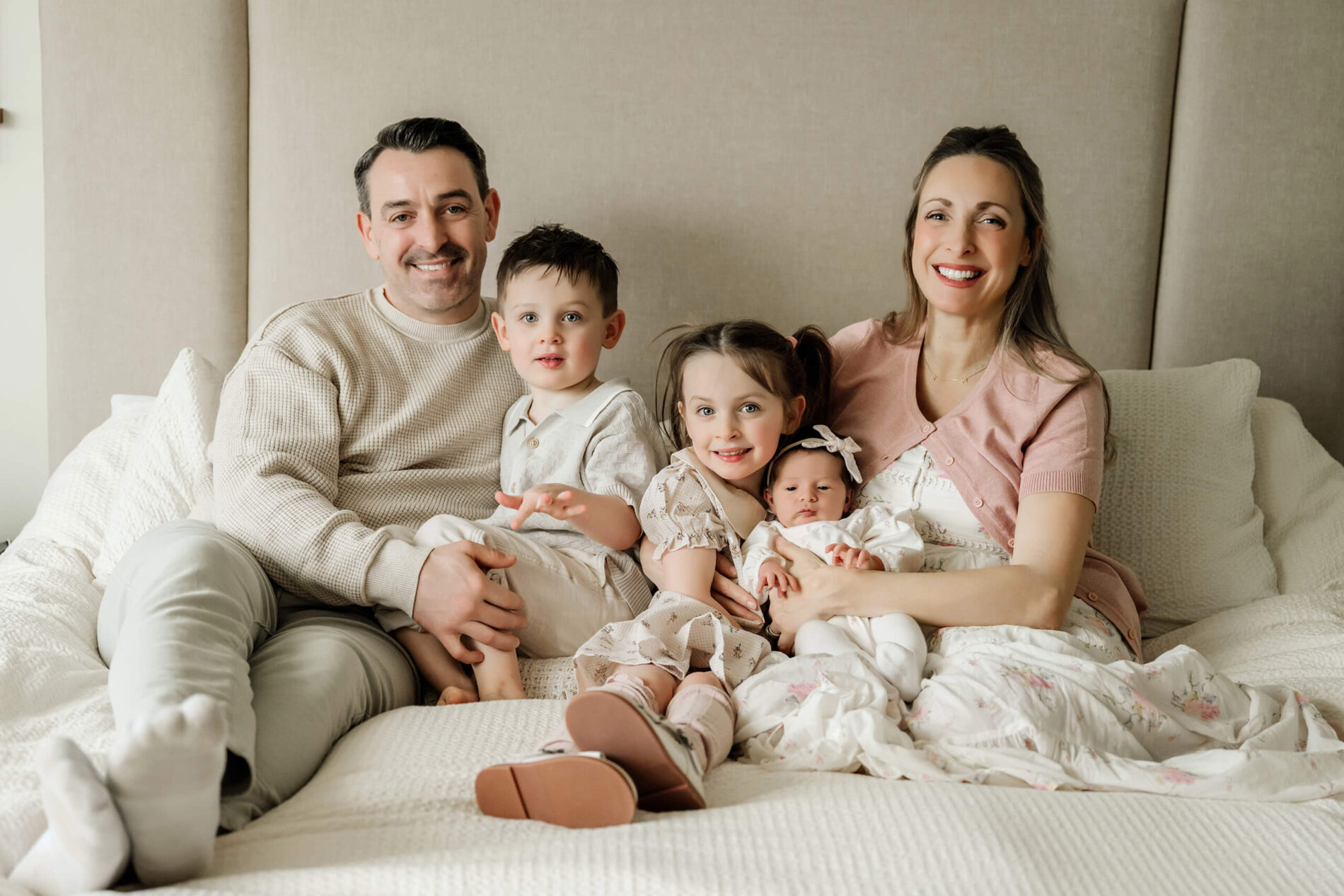 Parents sit on a bed with their two older children and newborn baby during an in-home family photo session.