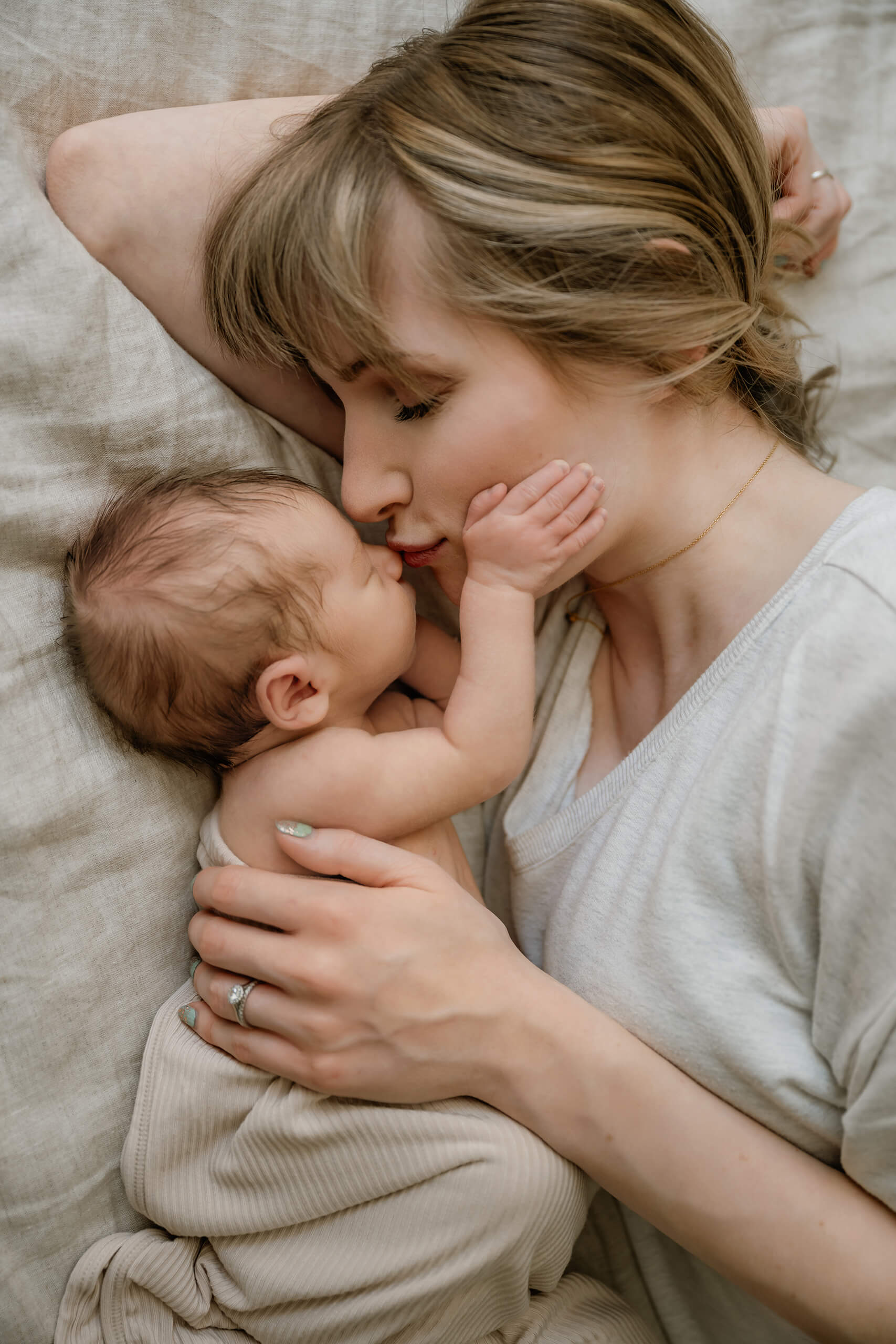 Close portrait of a mother kissing her newborn baby as the baby rests one hand against her cheek.