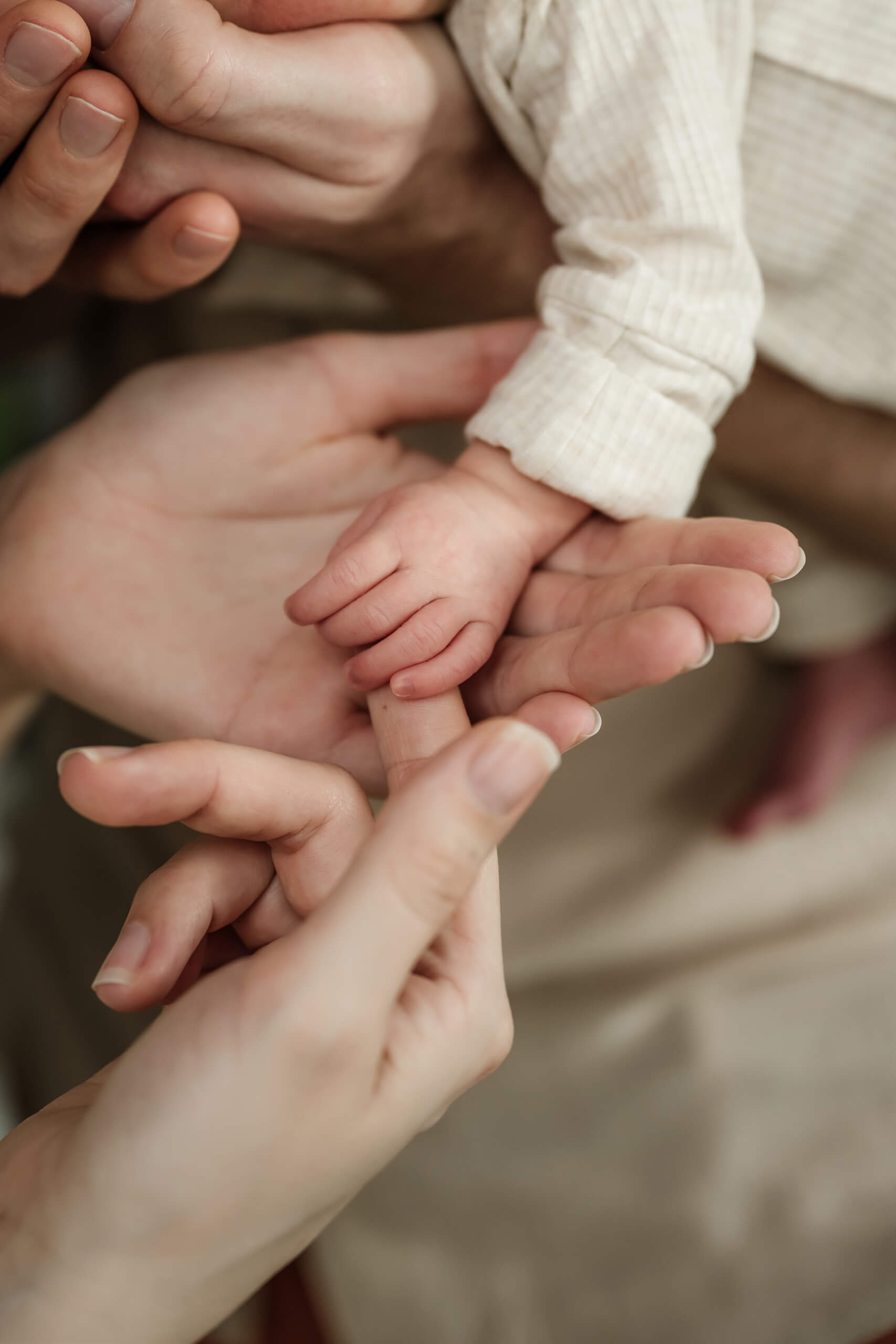 Close-up of a newborn baby’s hand resting across the open hands of both parents.