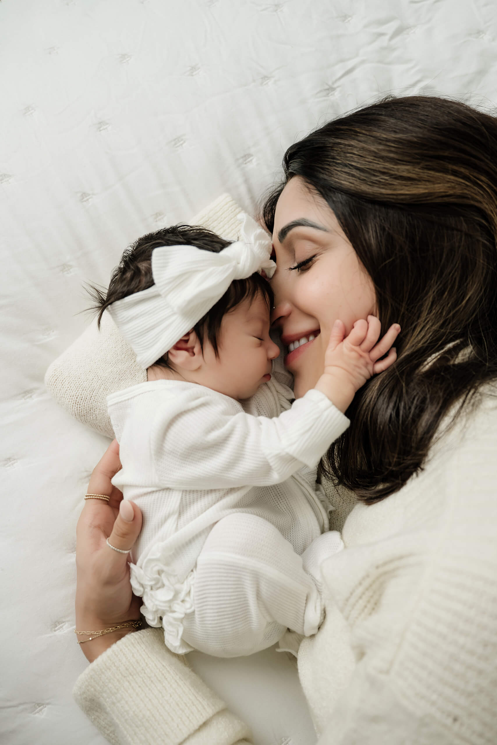 Mother cuddles her newborn baby cheek to cheek while lying together on the bed.