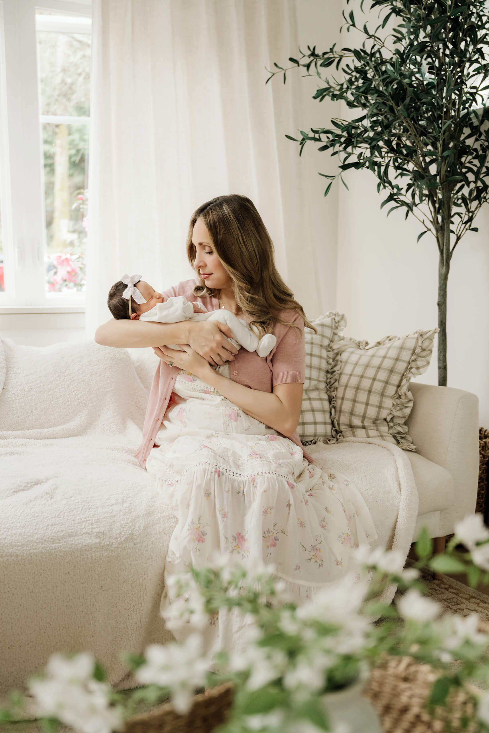 Mother holds and looks down at her newborn baby while seated in a bright living room.