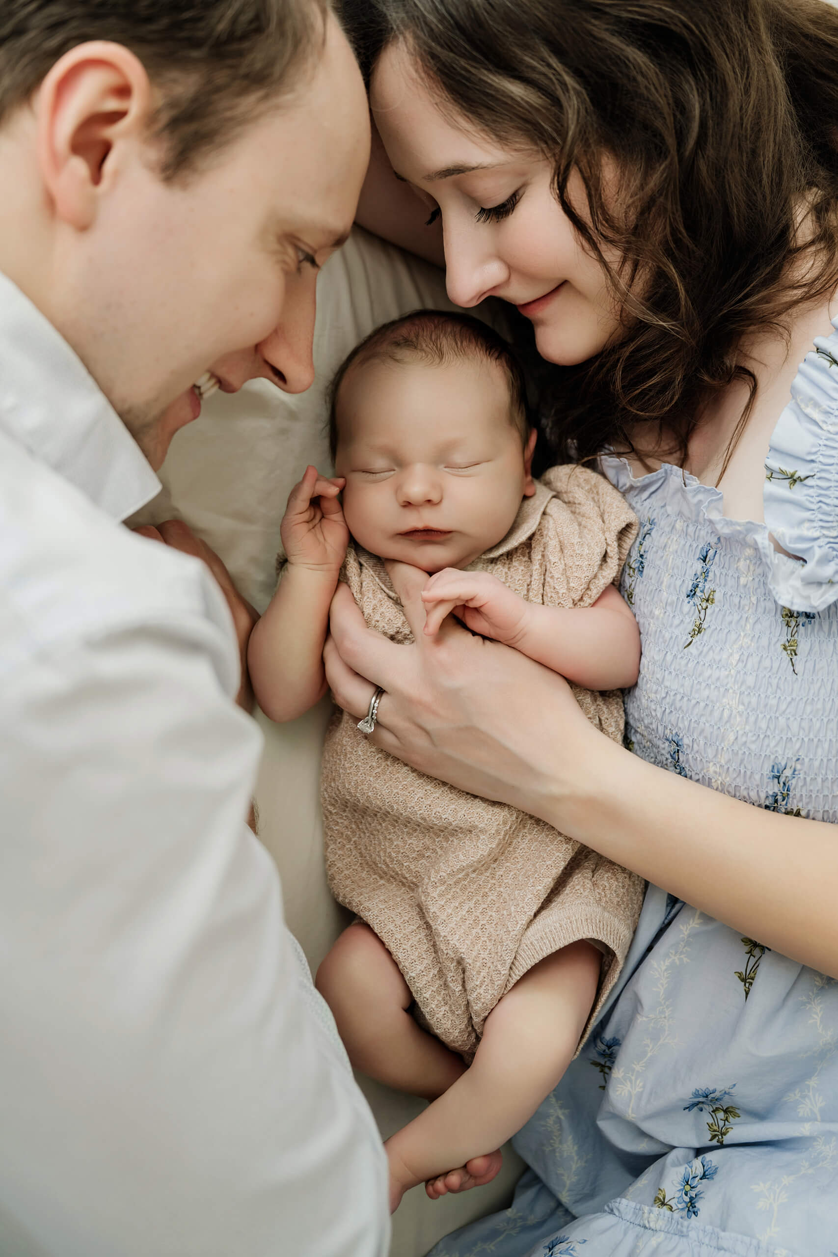Mother and father lean close around their sleeping newborn baby during an in-home session.