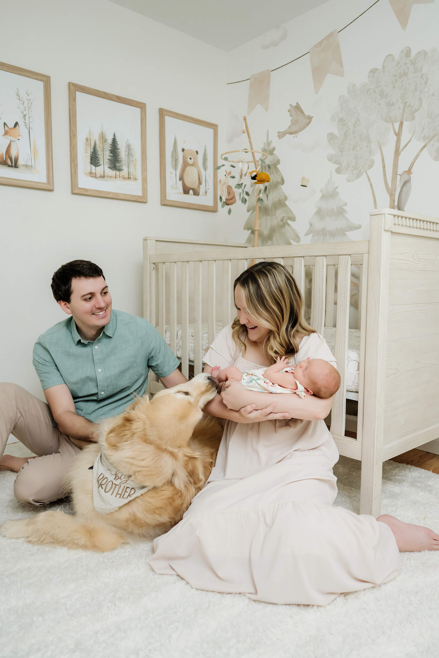 Parents sit with their newborn baby and golden retriever in a softly decorated nursery.