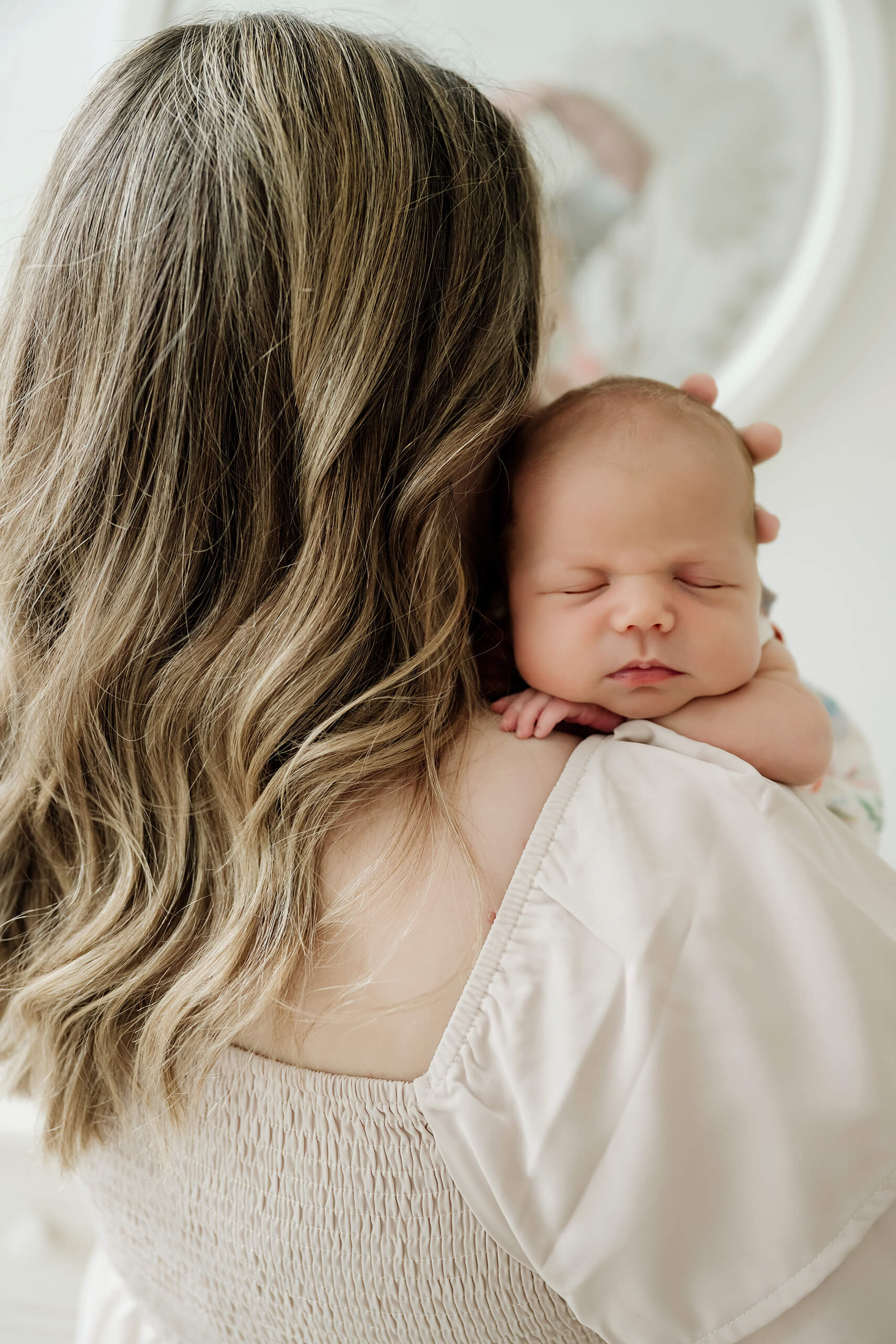 Sleeping newborn baby rests over her mother’s shoulder during an intimate in-home portrait.