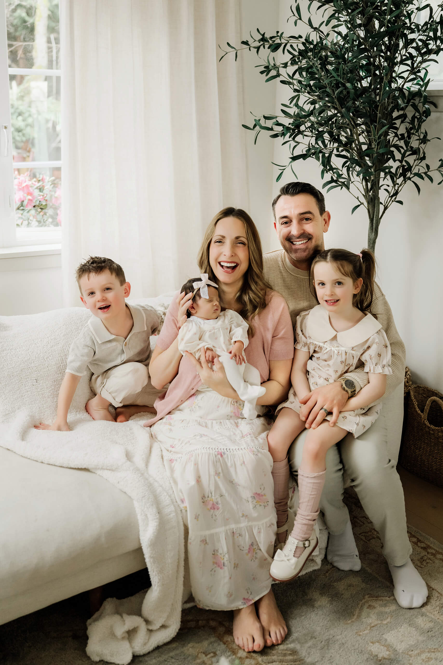 Family of five sits together on a living-room sofa with their newborn baby and two older children.