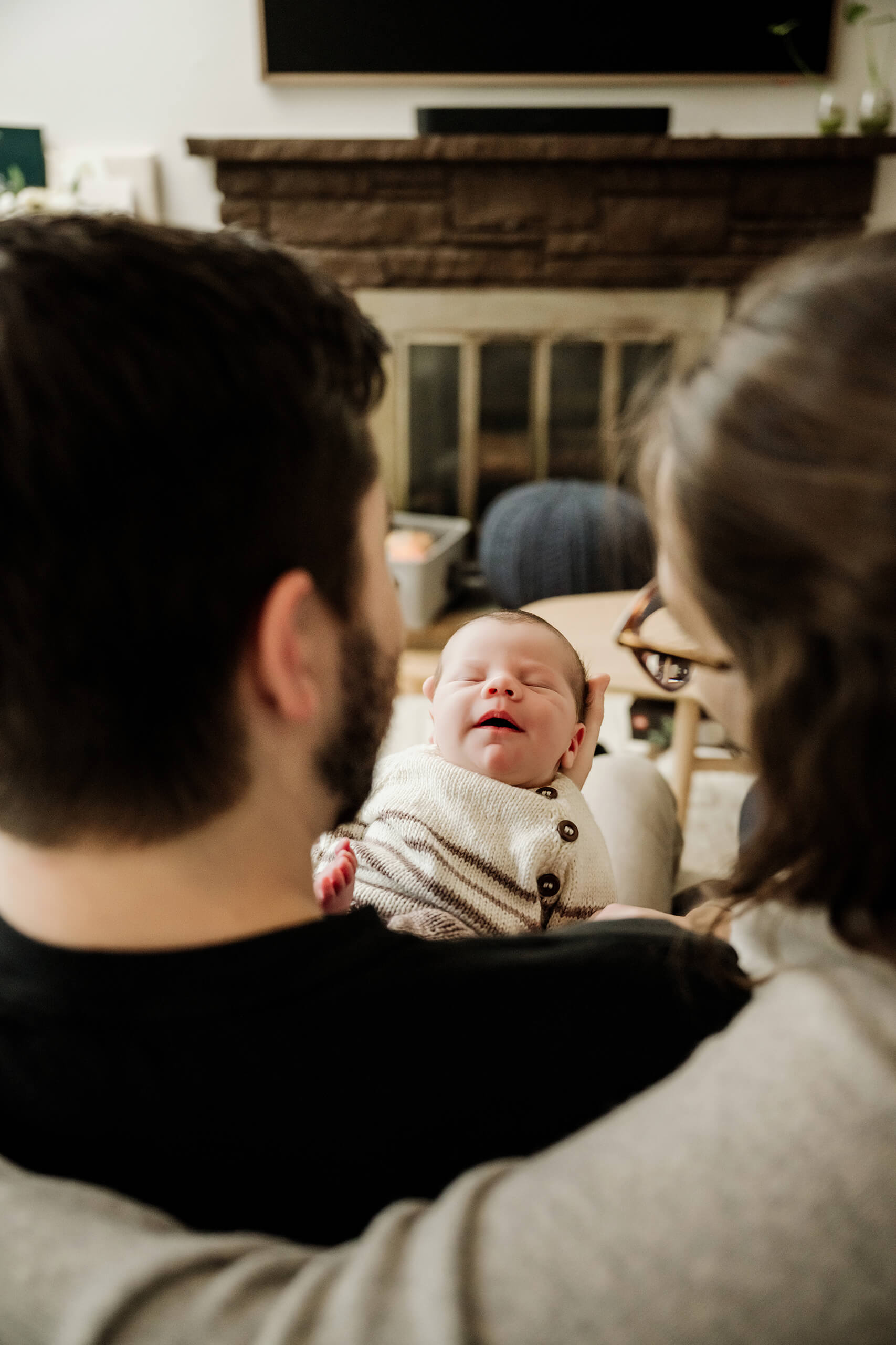 Mother and father look at their newborn baby resting between them during an in-home lifestyle session.