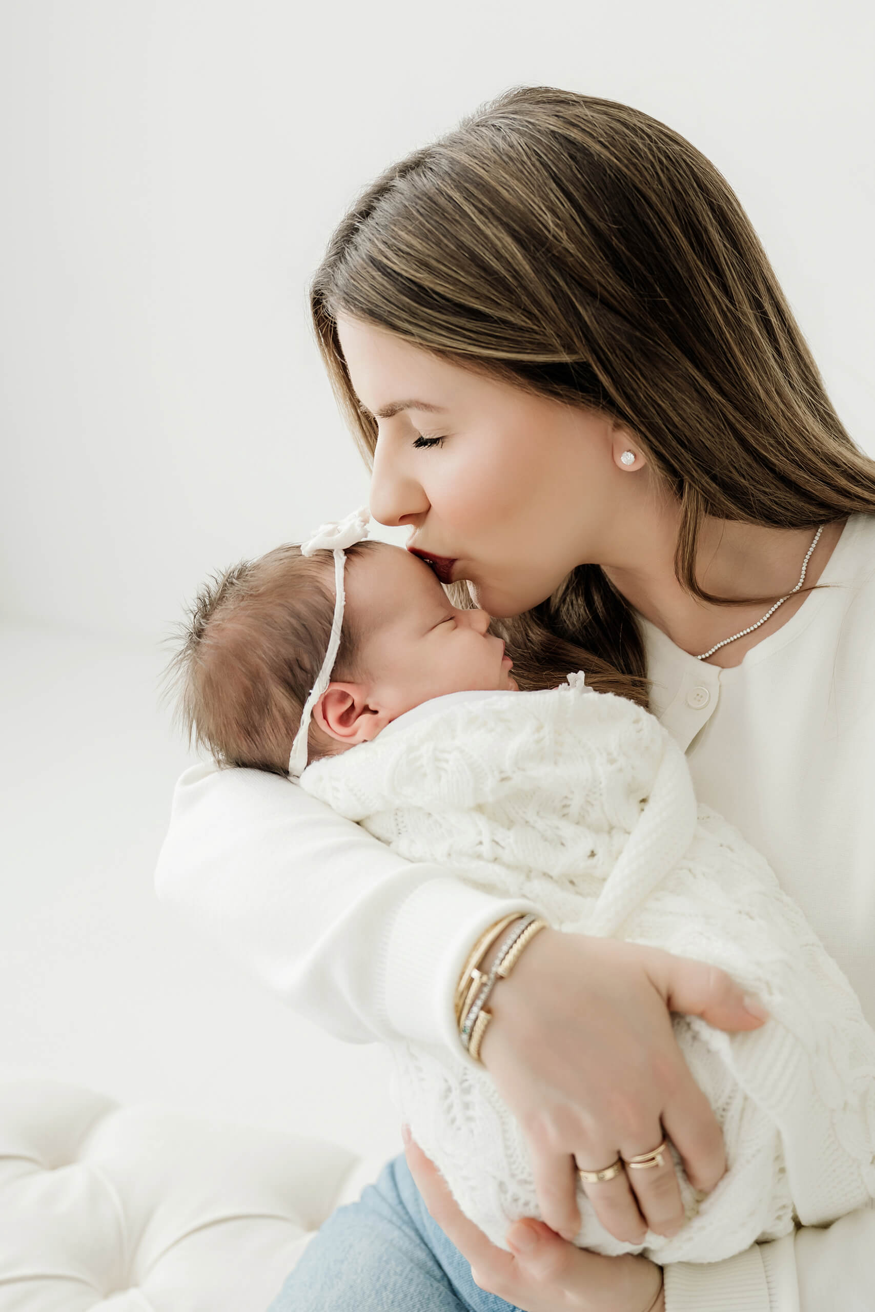 Parent kisses the forehead of a newborn wrapped in a white knit blanket.