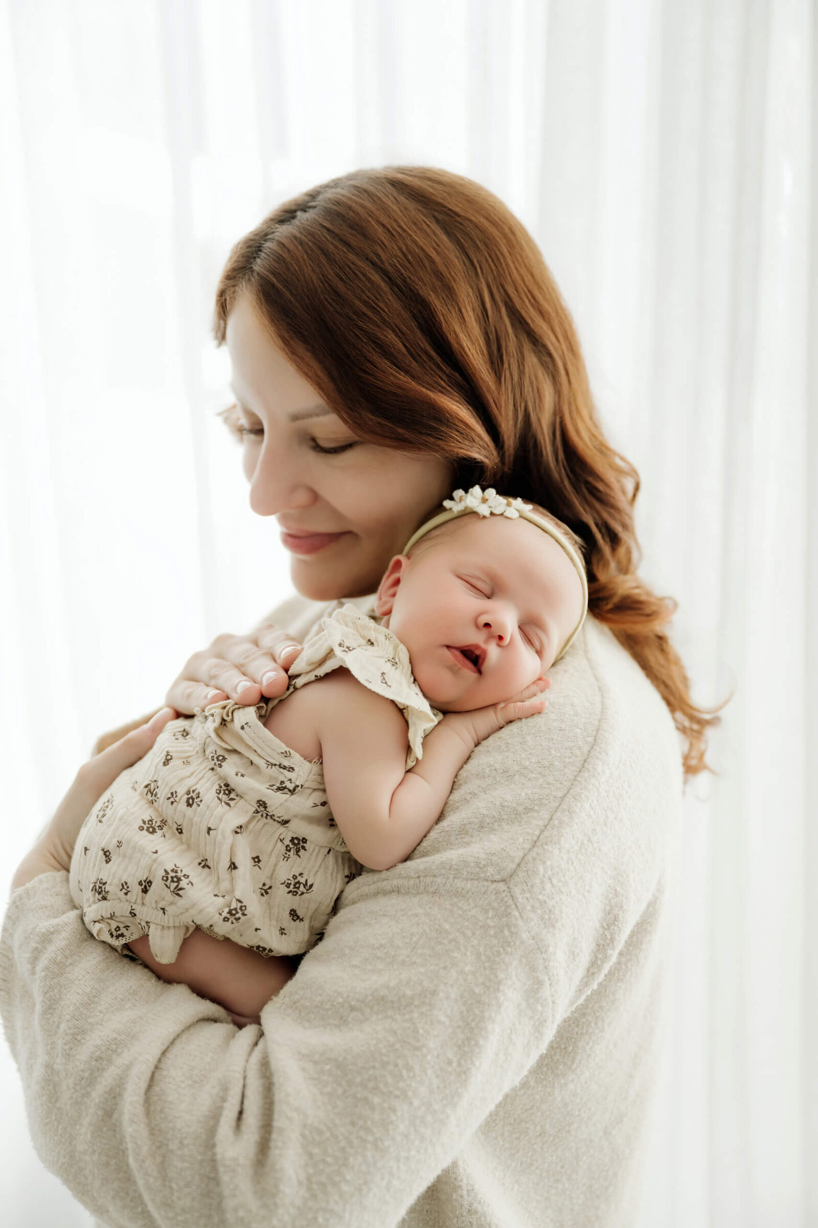 Parent holds a newborn against her shoulder, wearing a floral outfit and cream headband.