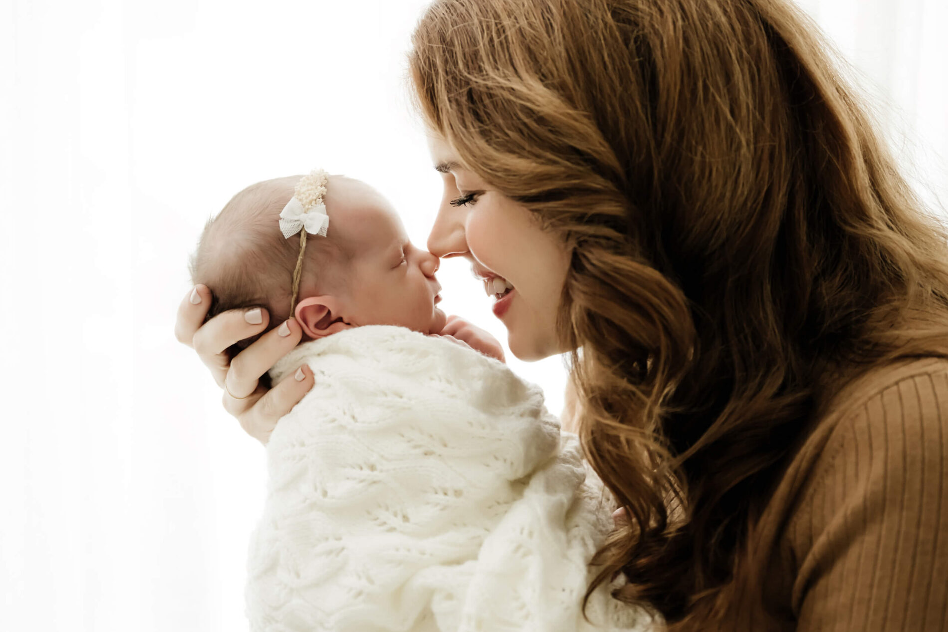 Parent supports a newborn’s head while leaning in nose to nose over a white knit blanket.