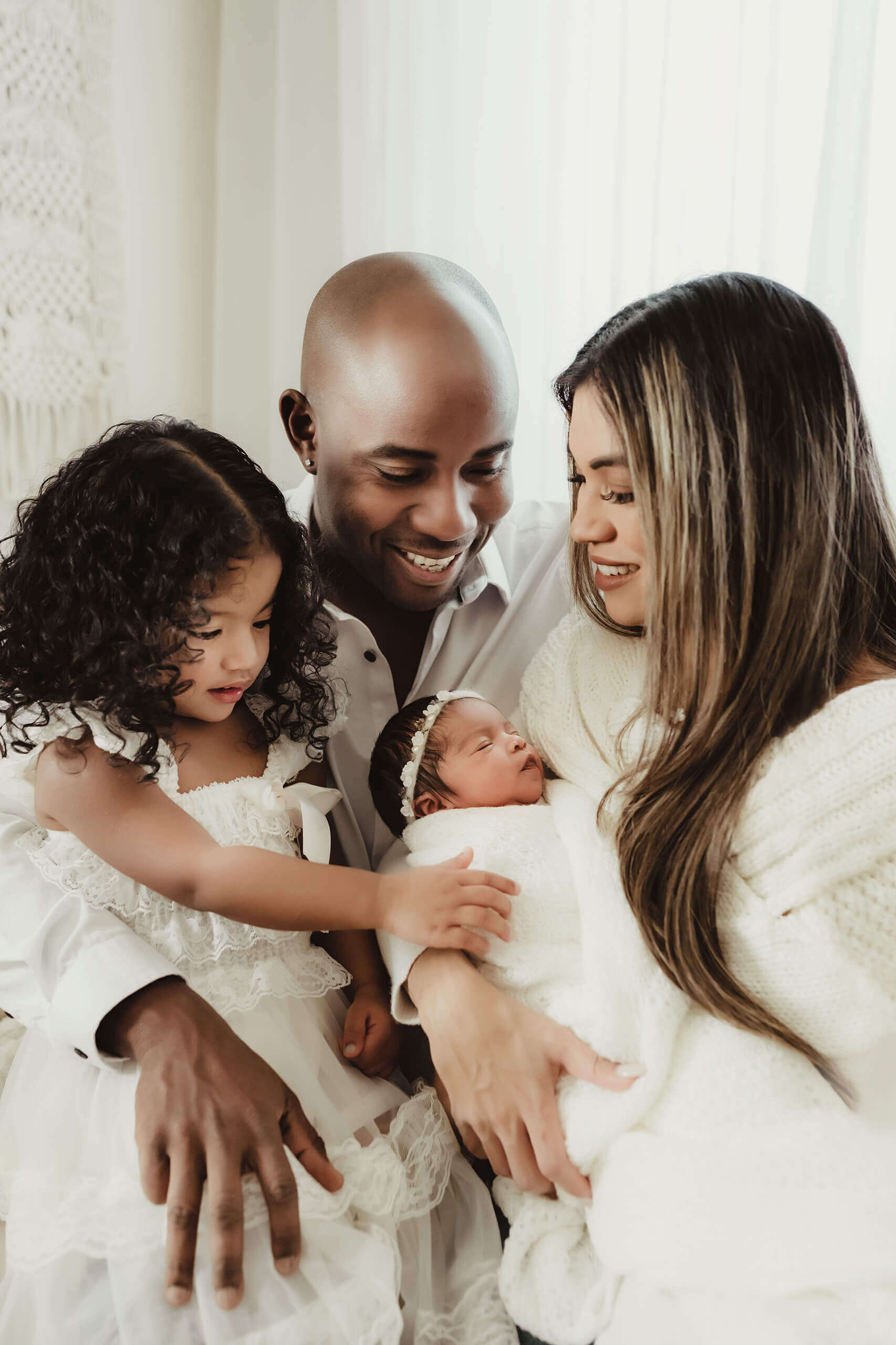 Two parents and a young sibling gather around a newborn bundled in white.