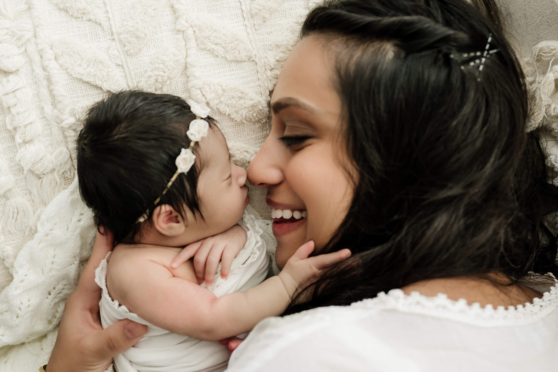 Smiling parent lies face-to-face with a newborn who reaches toward their cheek.
