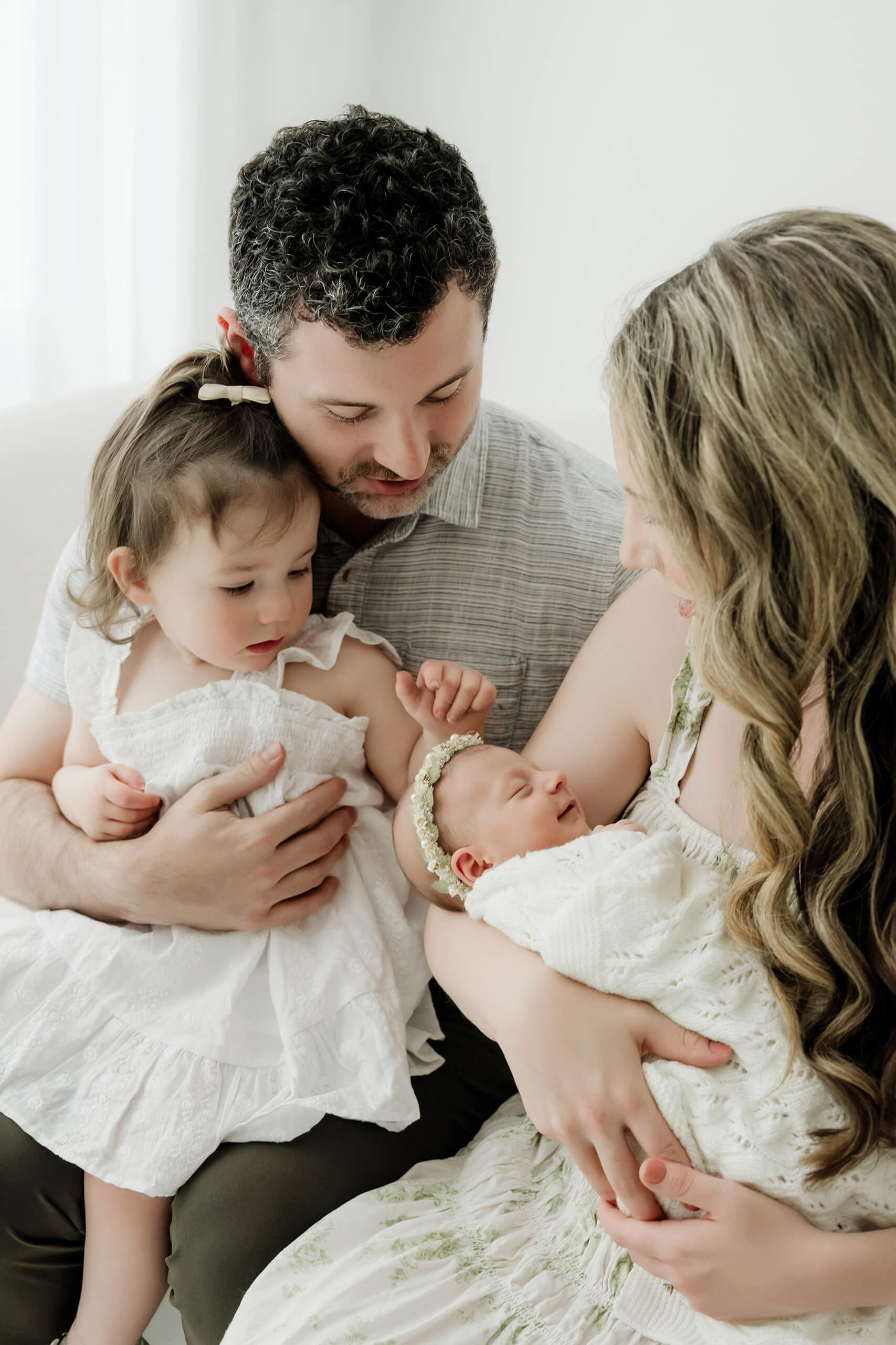 Two parents and a young sibling look down at the newborn cradled in one parent’s arms.