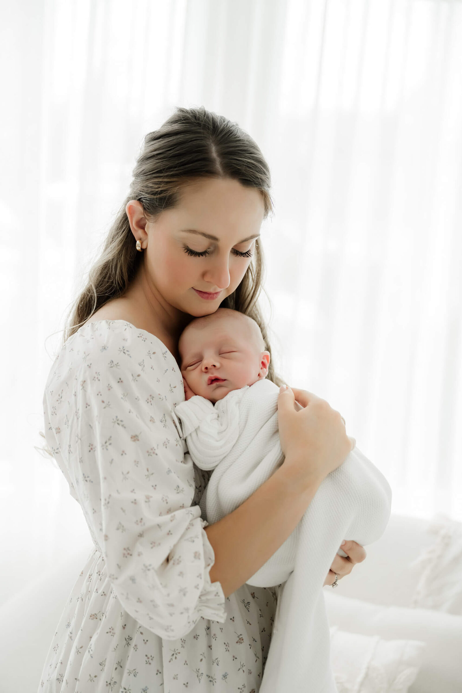 Parent holds a newborn with eyes closed against their shoulder in a white knit outfit.