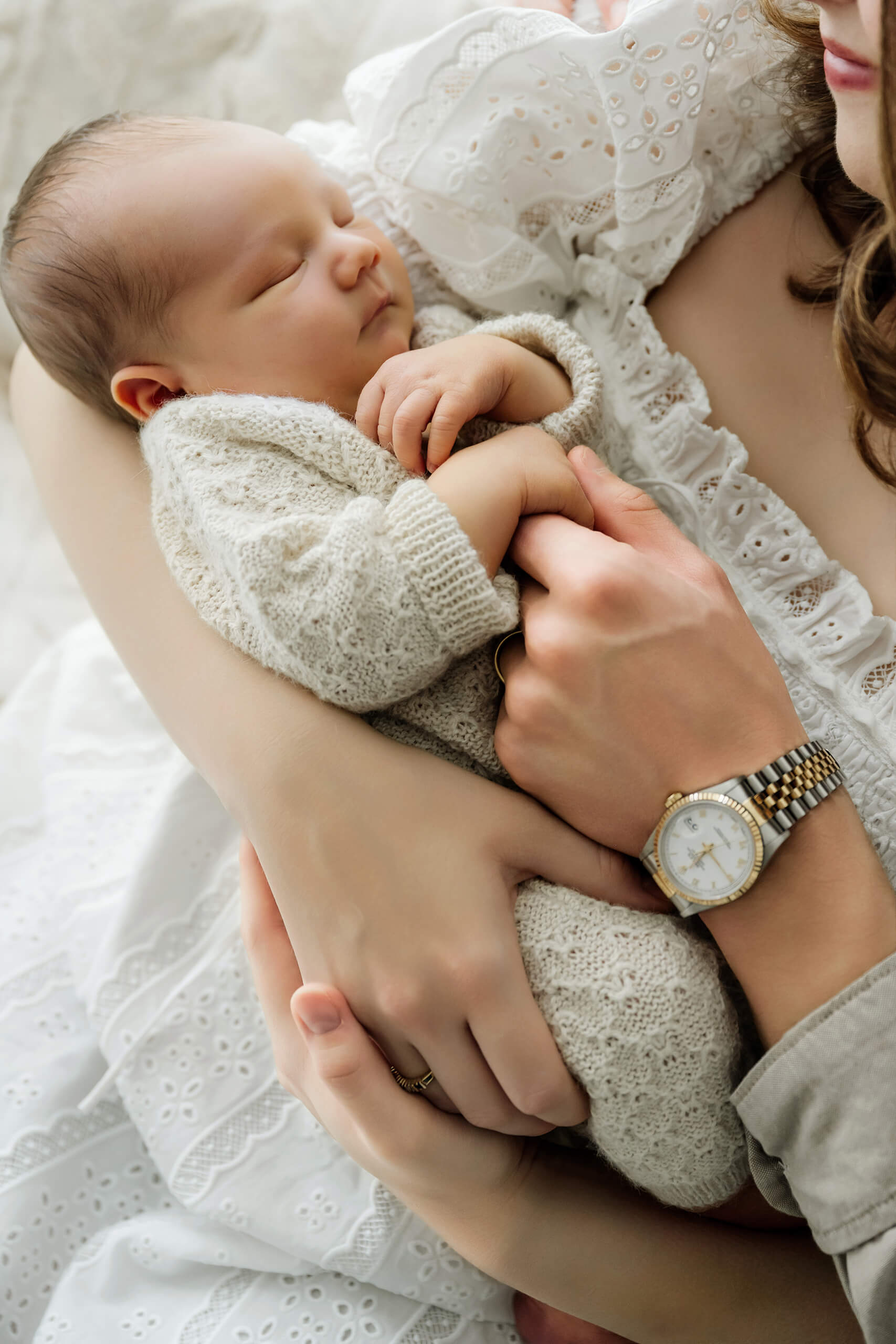 Sleeping newborn in a gray knit outfit rests securely in the parents’ arms.