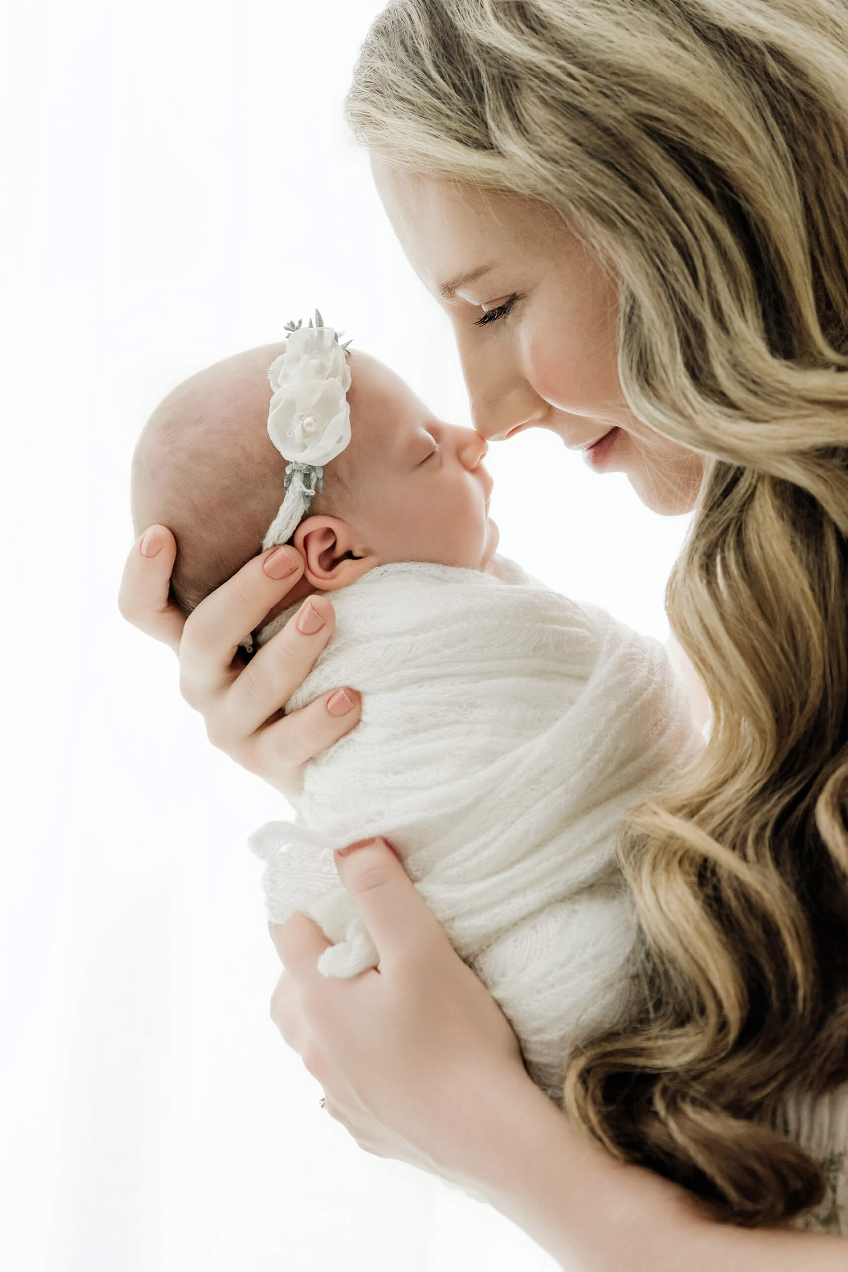 Mother holds her swaddled newborn close and gently touches noses with the sleeping baby.