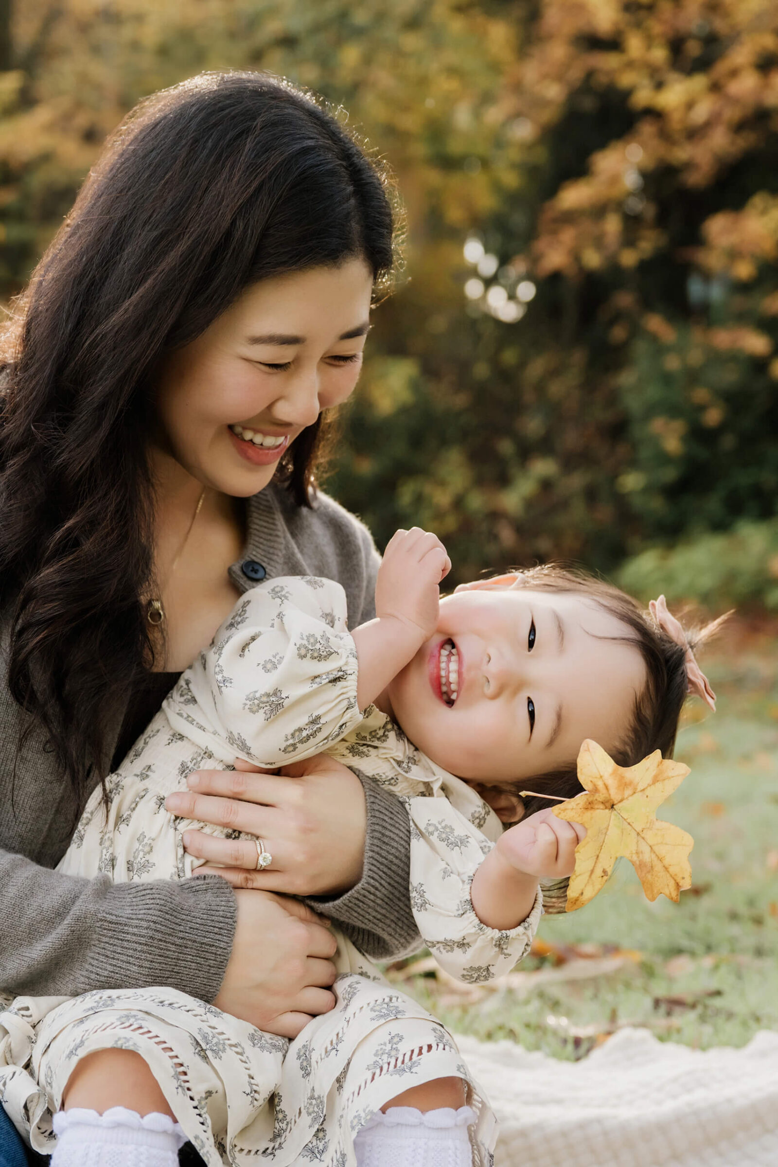 Mom holds her smiling daughter as she shows a large yellow fall leaf.