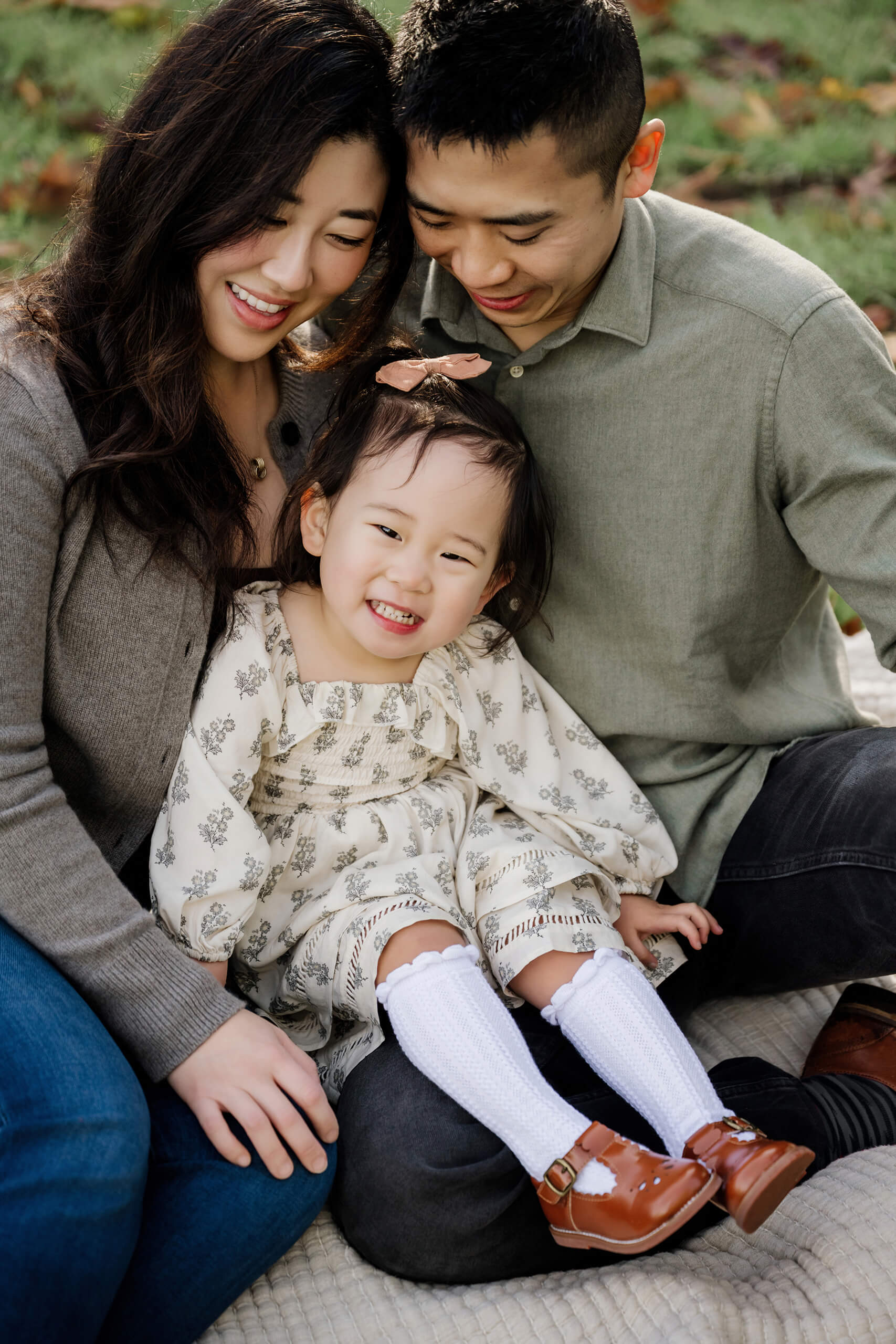 Close portrait of parents leaning toward their smiling daughter during an outdoor fall family session.