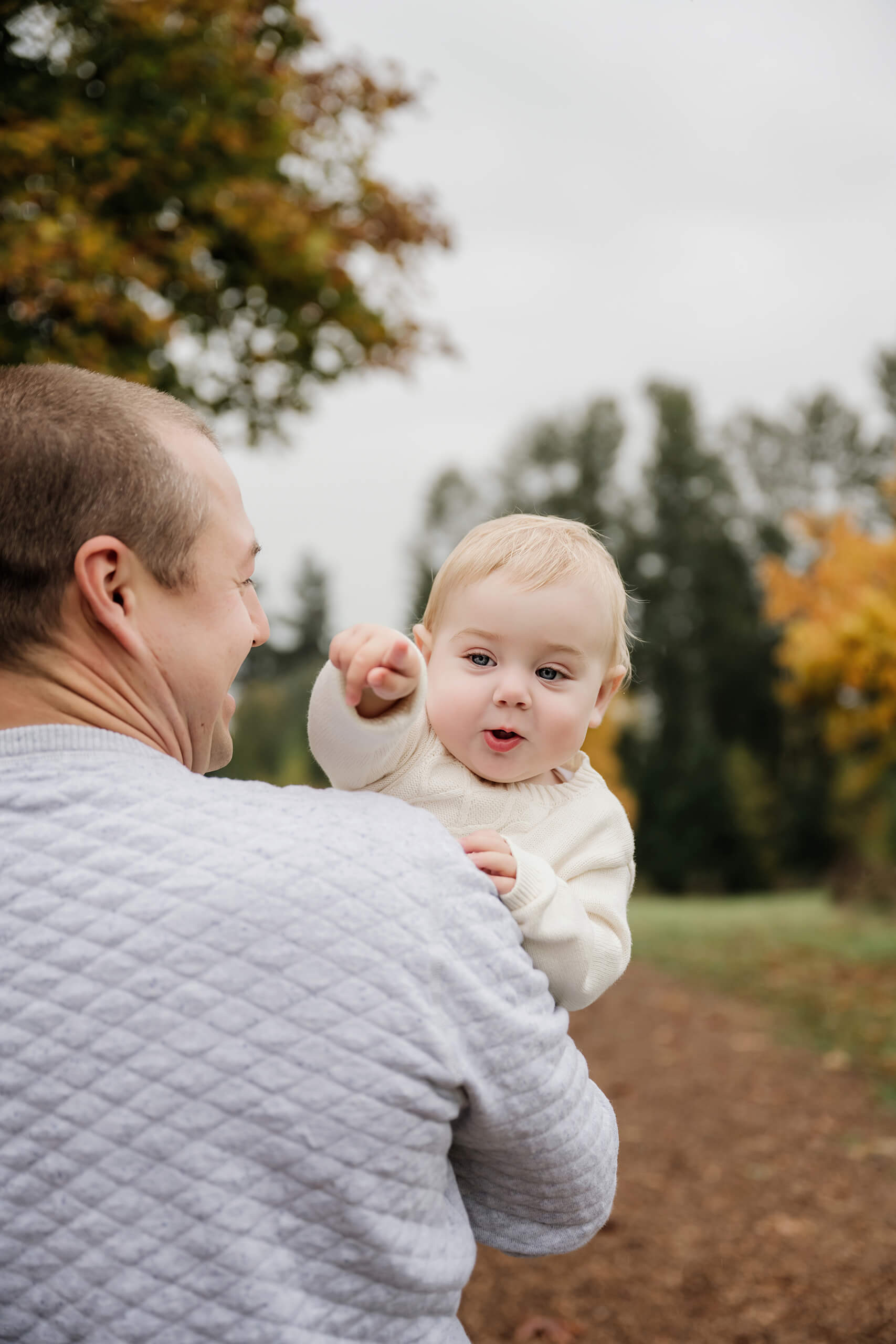 Dad holds his baby as she points toward something during their outdoor fall family session.