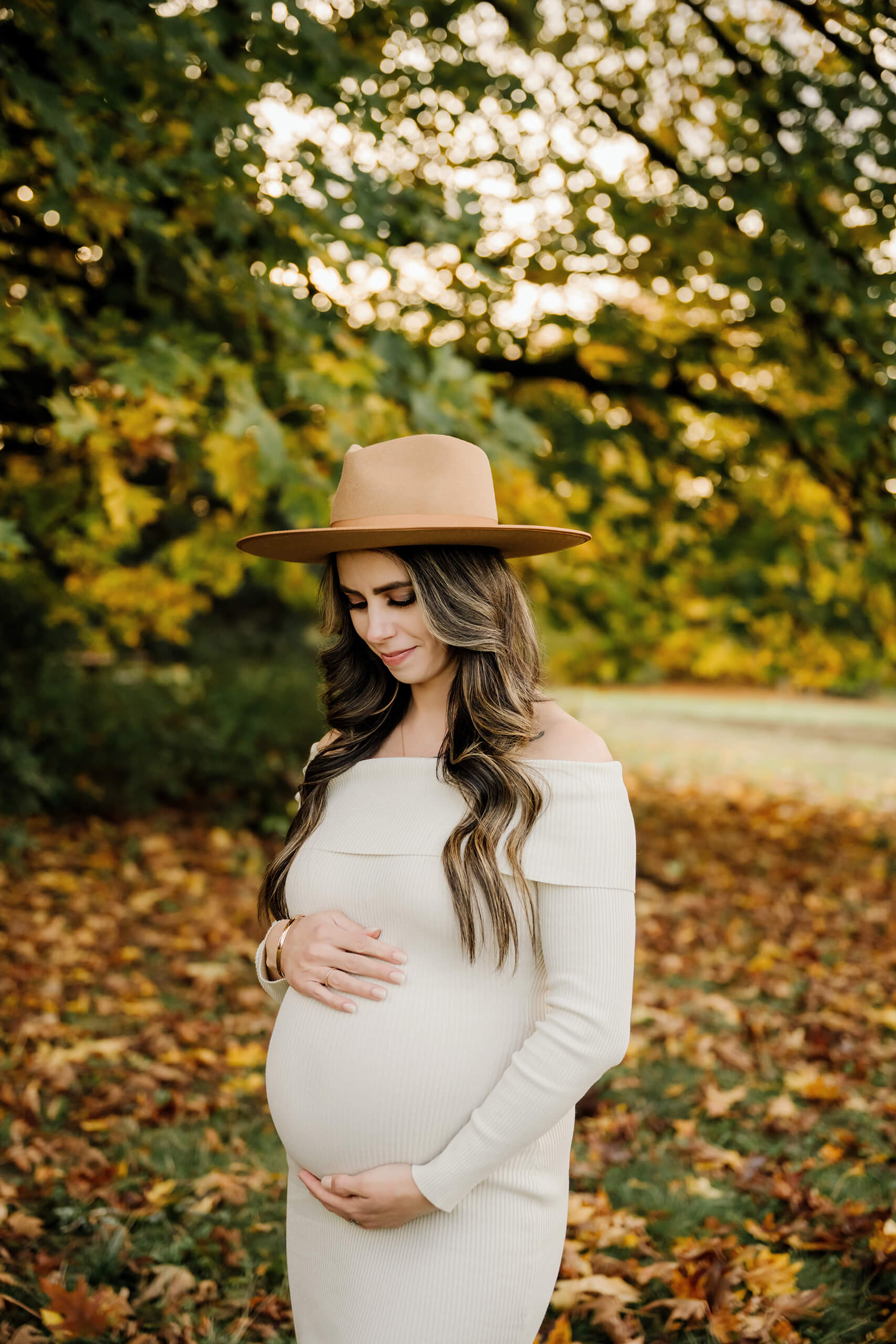 Expecting mom cradles her belly beneath a canopy of green and yellow fall leaves.