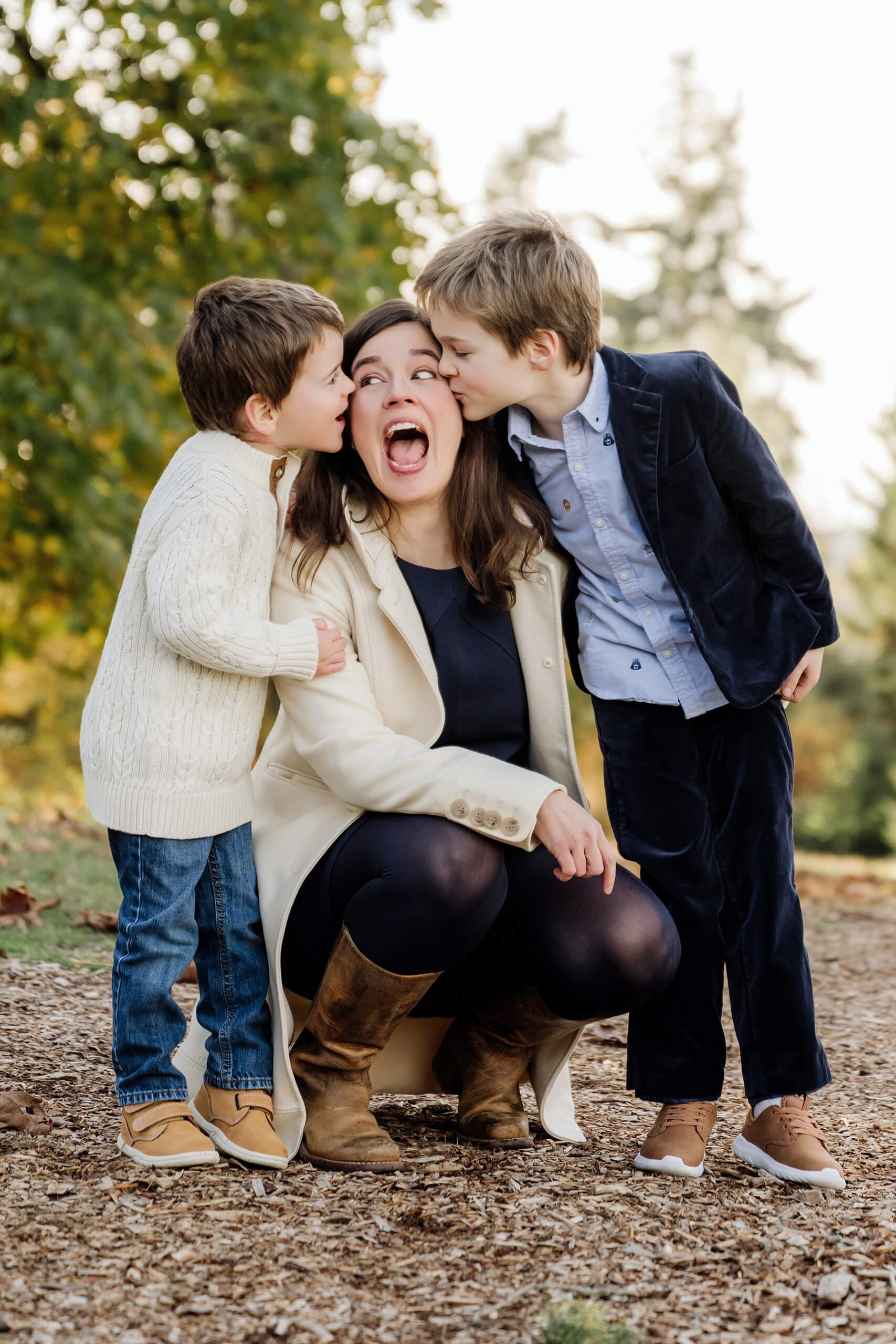 Two sons kiss their mom on the cheeks during a playful fall family portrait.