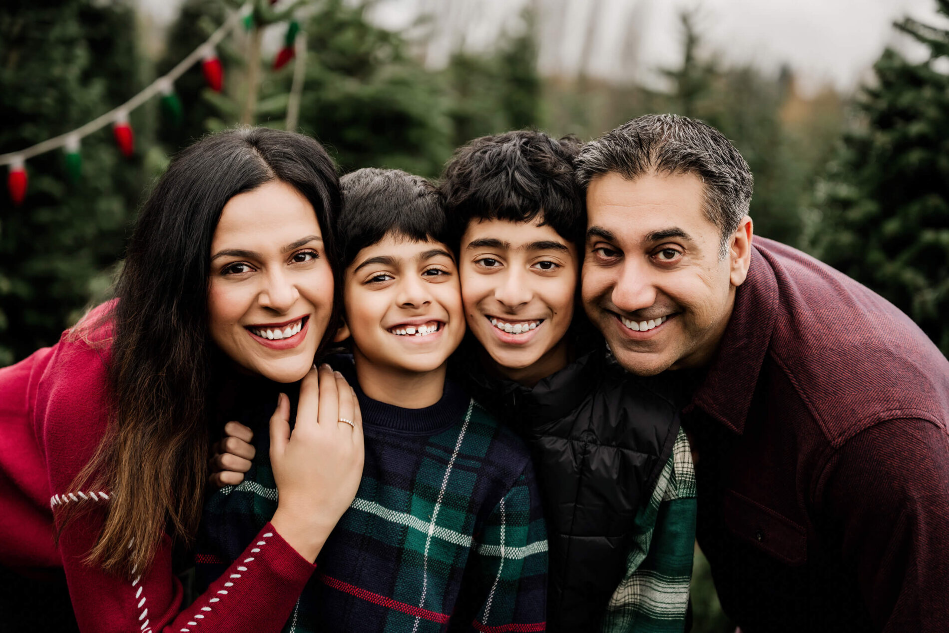 Mom, dad, and their two sons press close together and smile at the camera in a tight family portrait.