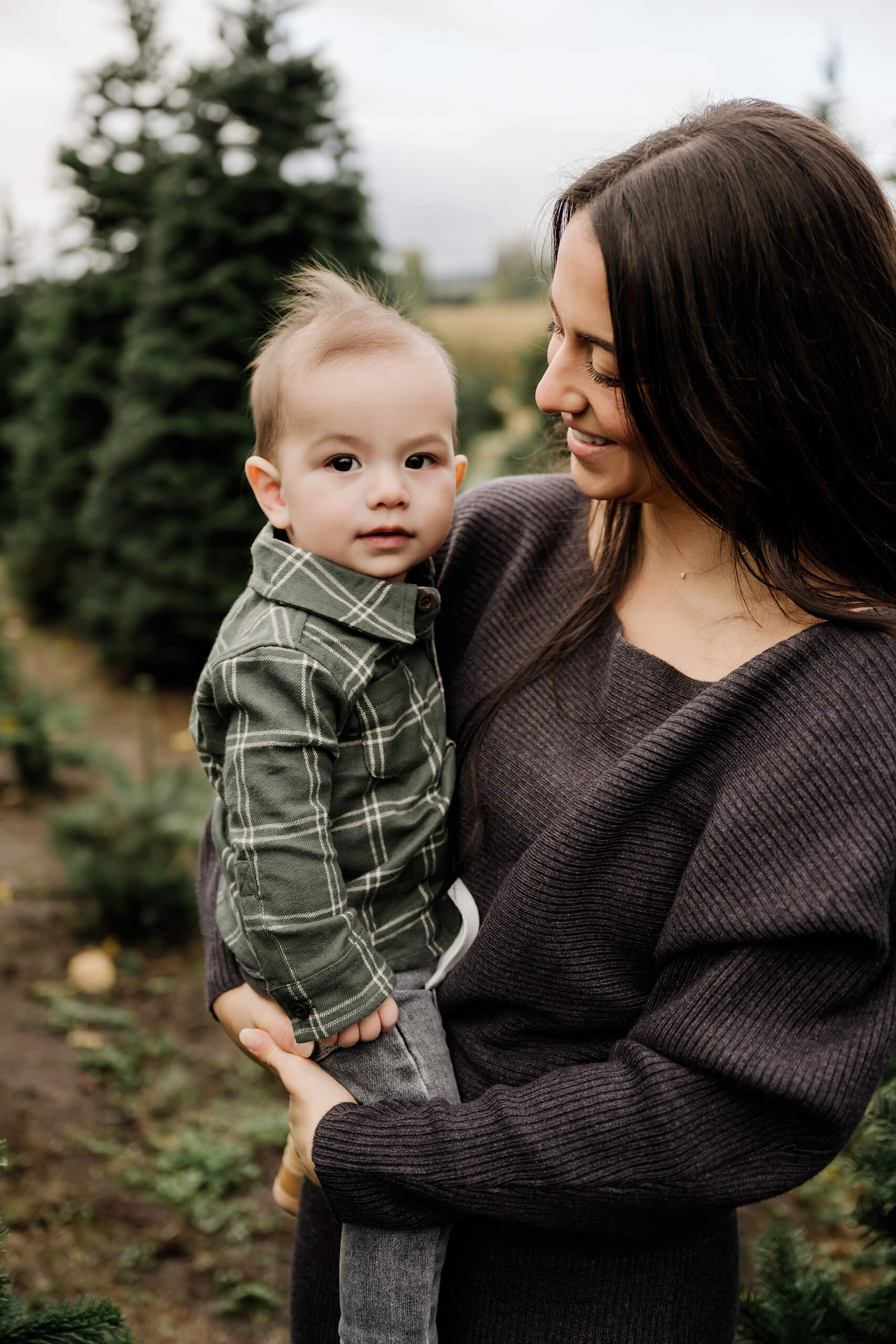 A mom holds her son and smiles down at him as he looks toward the camera.