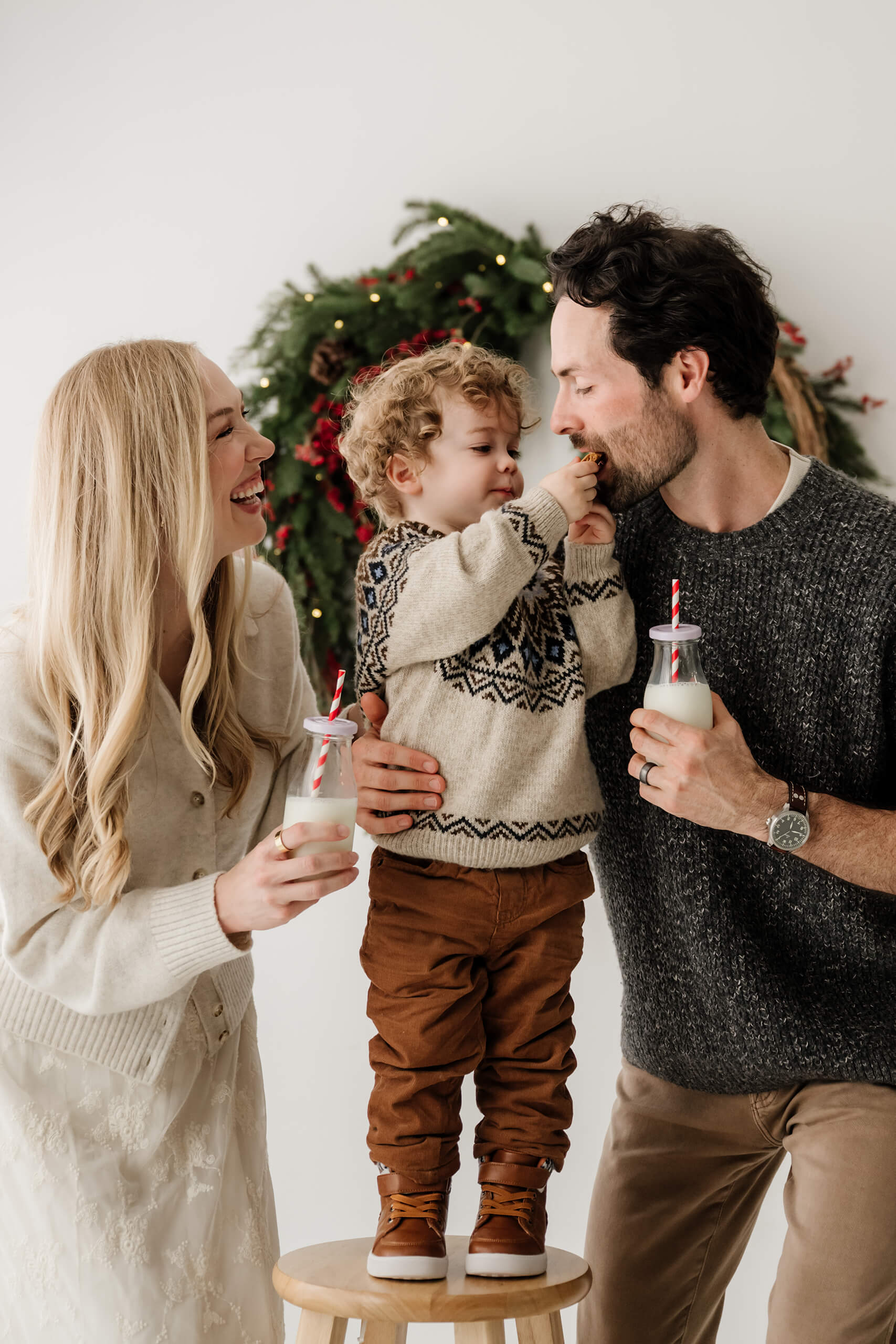 Mom and dad sharing milk and cookies with their son as he feeds dad a cookie.