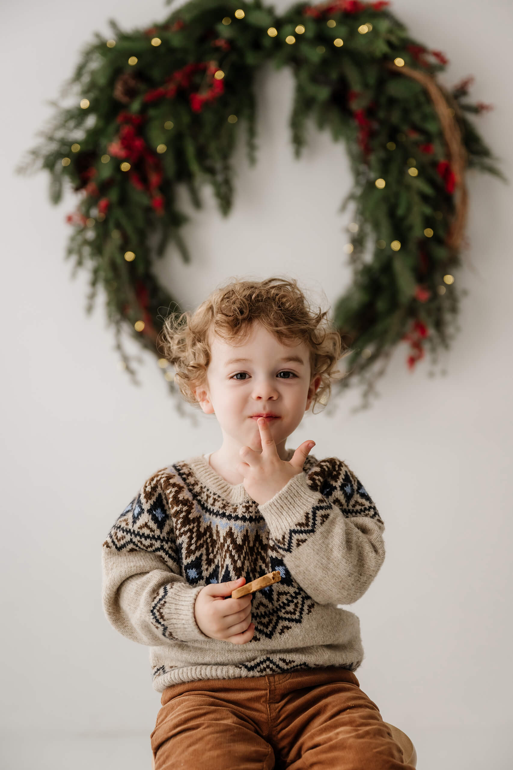 Young boy holding a cookie beneath the softly blurred holiday wreath.