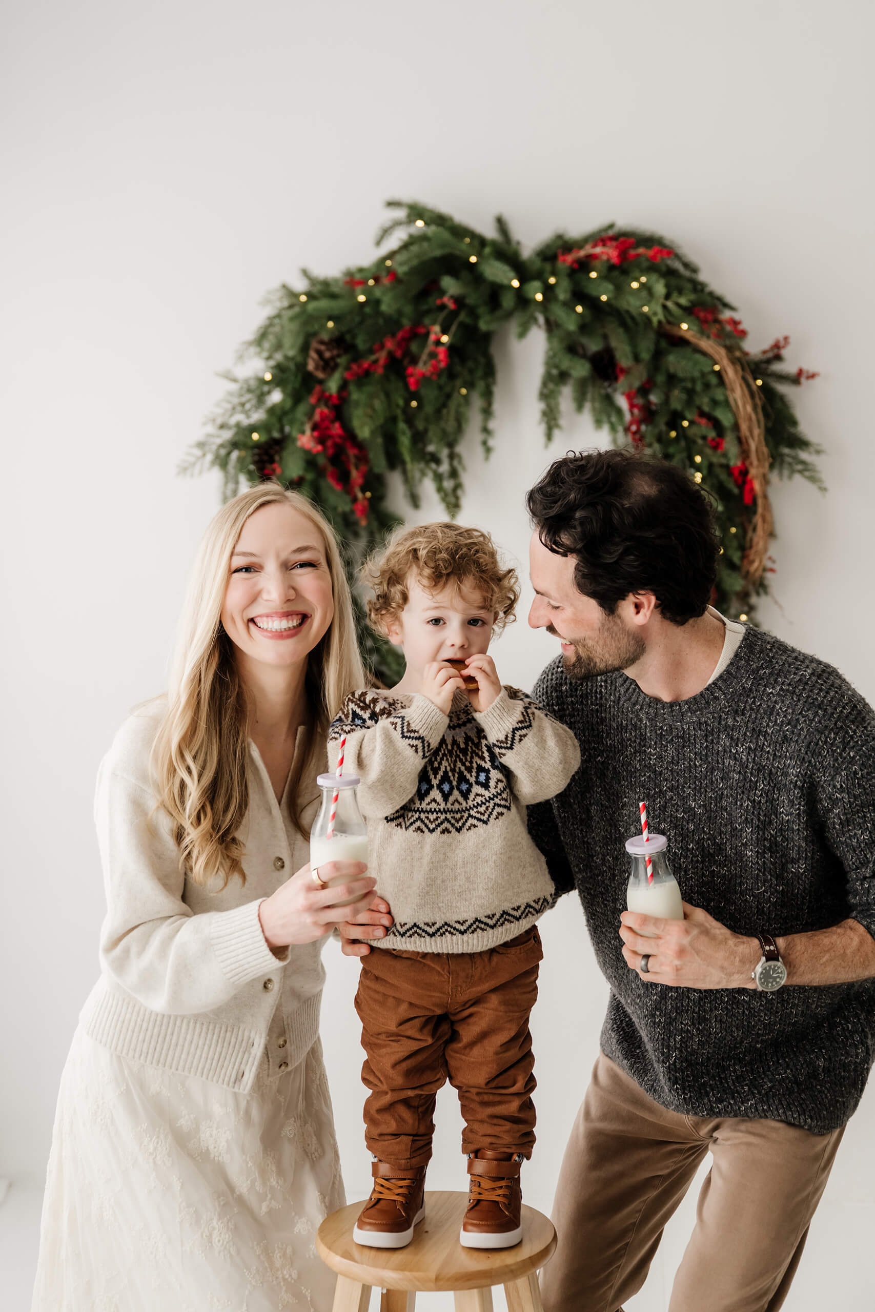 Mom and dad gathered around their son during a milk-and-cookies moment beneath the evergreen wreath.